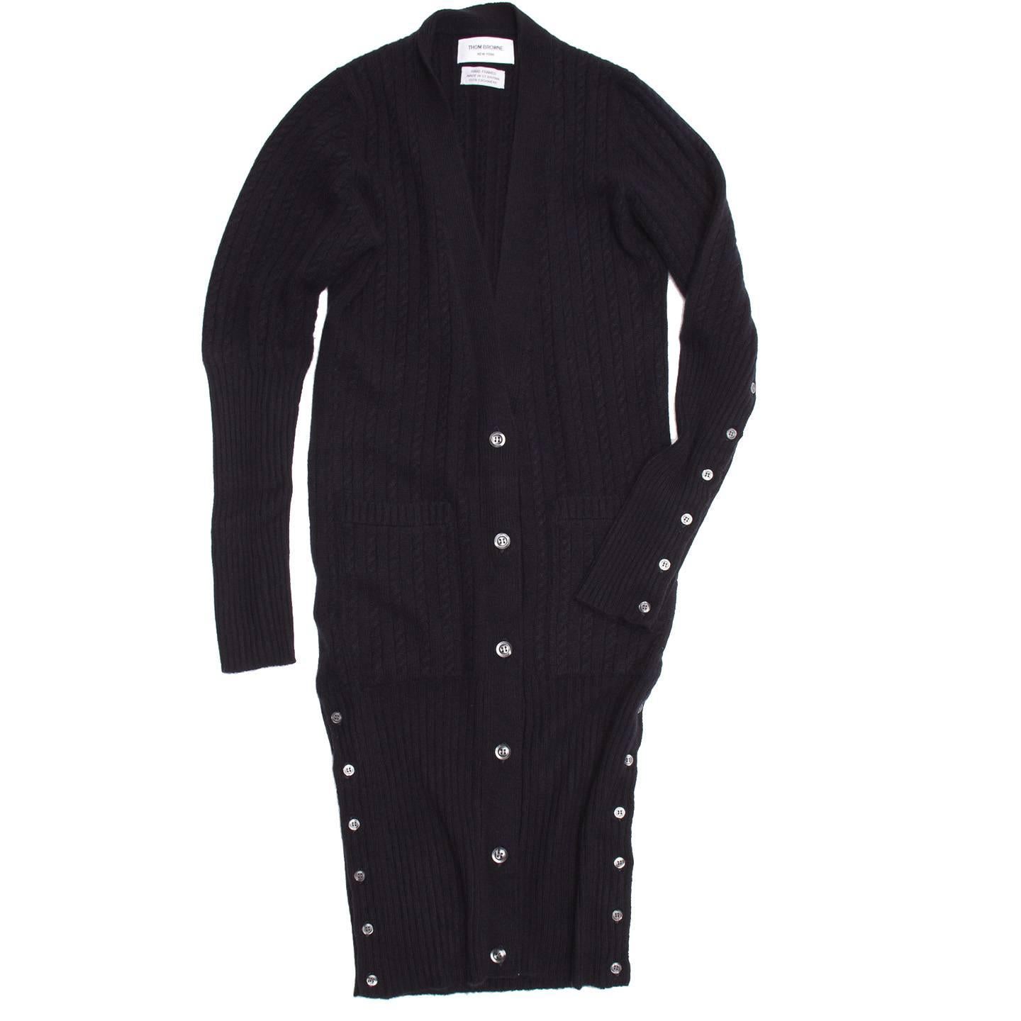 Hand framed navy blue cashmere cable knit V-neck dress or oversized cardigan with two little pockets at hips. It is a knee length cardigan with front, cuffs and hem that fasten with dark grey buttons and show a blue/red/white striped ribbon when