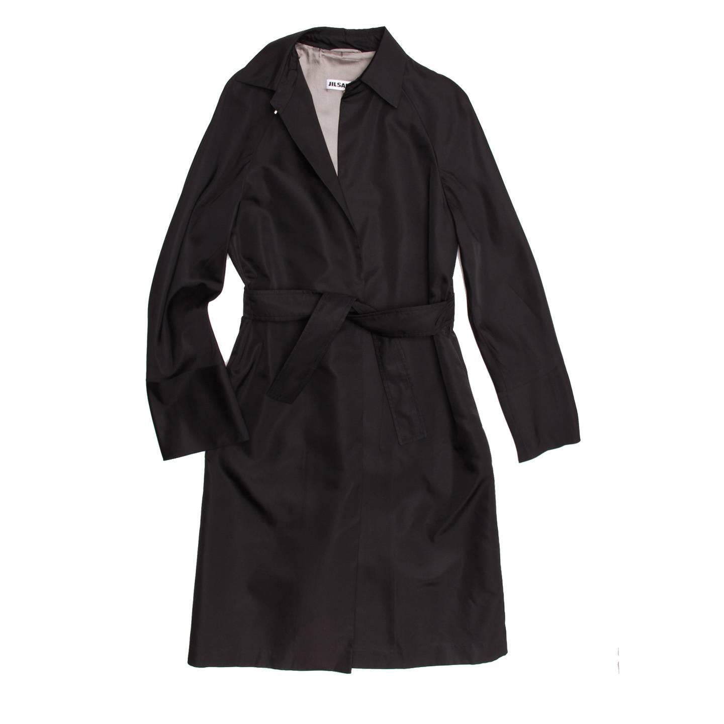 Black silk evening style trench coat. Single button closure at waist with self fabric belt at front. Raglan sleeves and hook and eye closure at center front neckline. A-line silhouette and back flange detail at back yoke.

Size  40 French