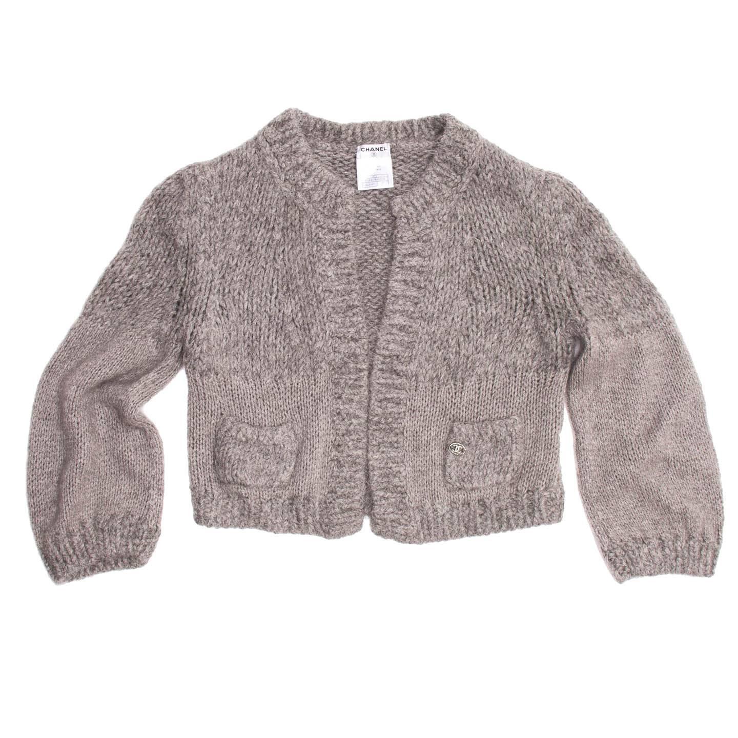 Melange grey angora/cashmere/chinchilla blend cropped cardigan with free open front. The collar has a classic Chanel round line and two mini patch pockets enriched by a beautiful jewel Chanel logo prettify the front of the cardigan.

Size  42 French