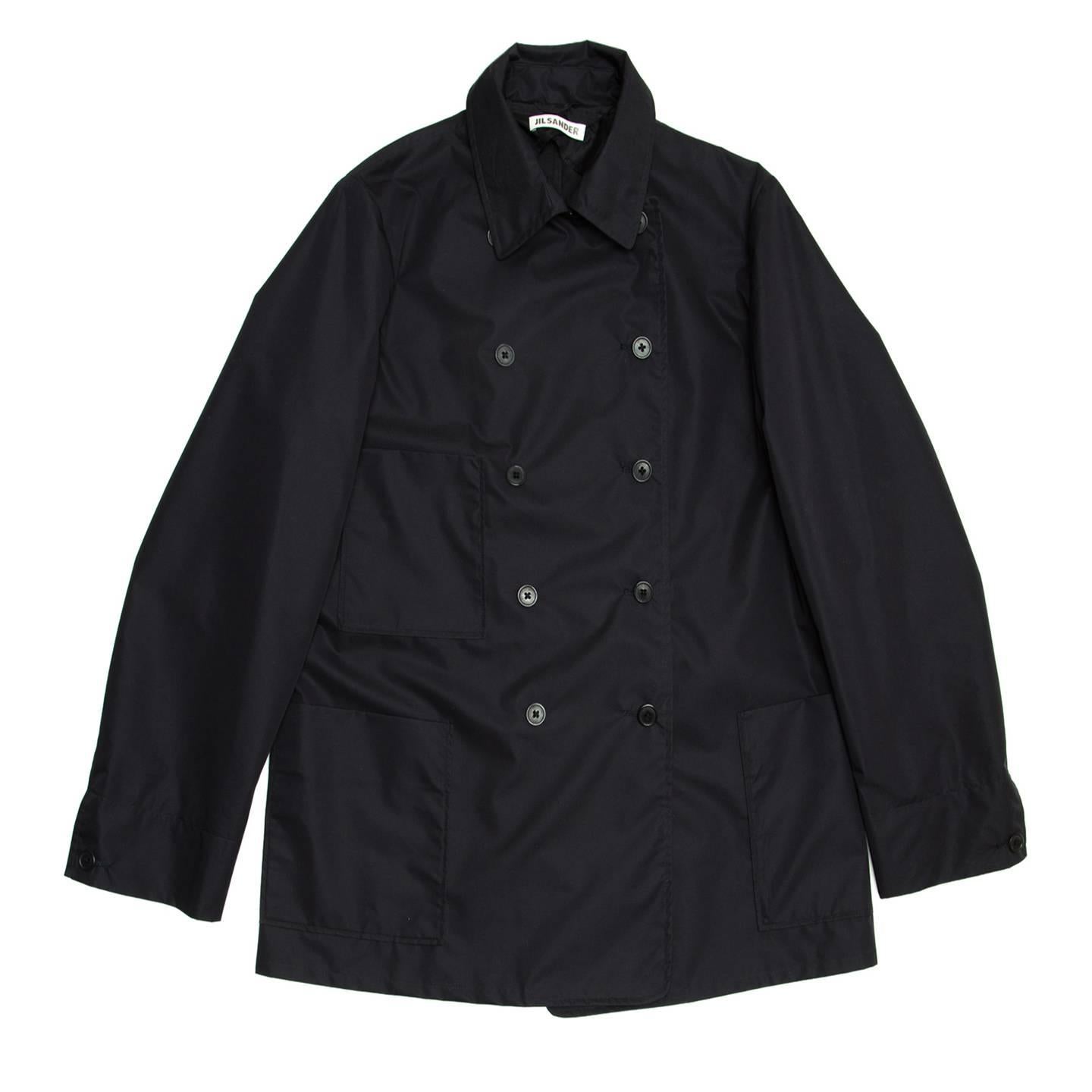 Cotton and polyester navy double breasted, boxy, middle length raincoat. 3 front big and squared patch pockets. Sleeves finish with cuffs that fasten with a brown button while the back is plain. The fabric of this coat is really light, waterproof