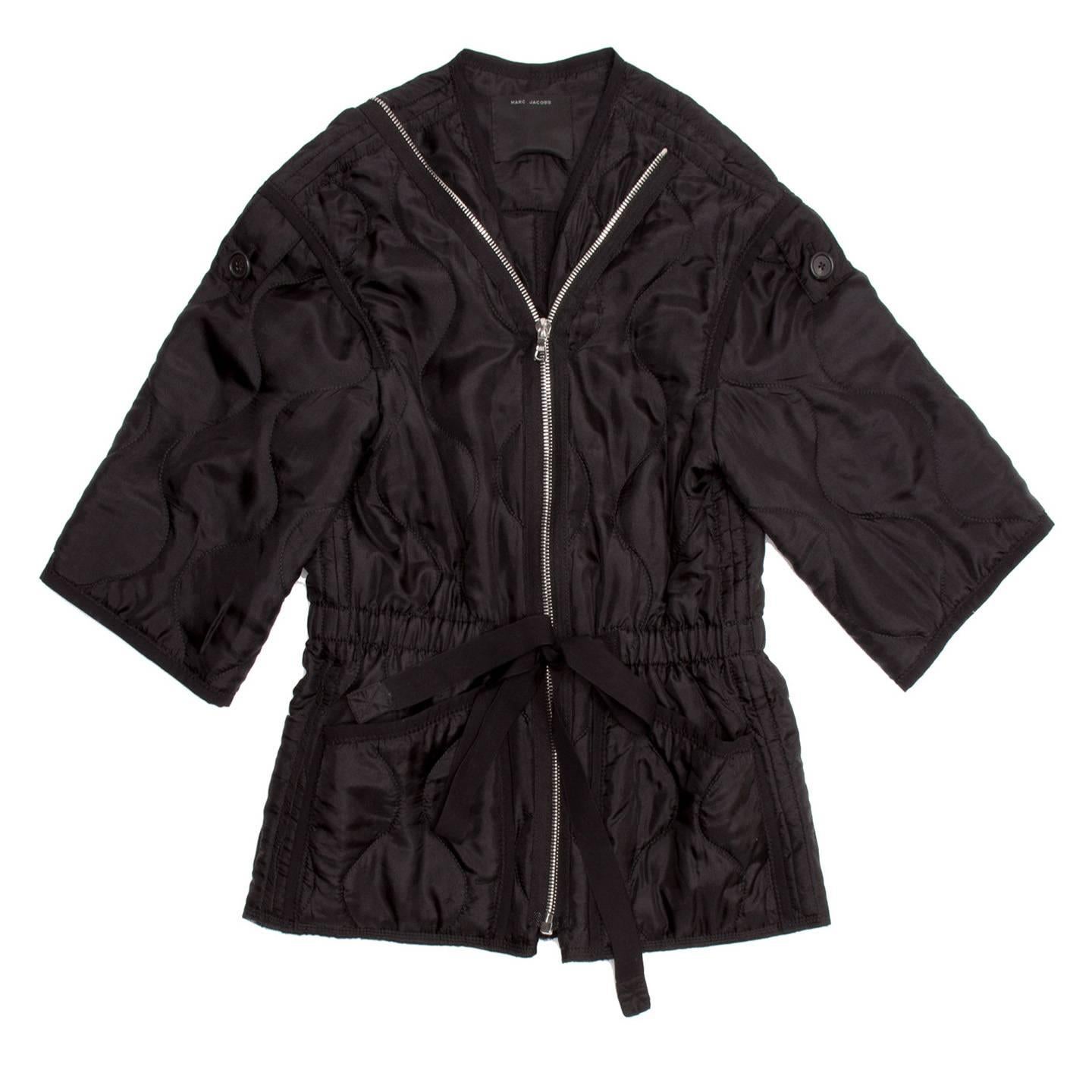 Black quilted jacket with cinched tie waist and 3/4 kimono sleeves. The Jacket is collarless and has two fastening systems: with two rows of buttons or with two zippers. The same black ribbon of the cinched tie waist adorns neck, patch pockets,