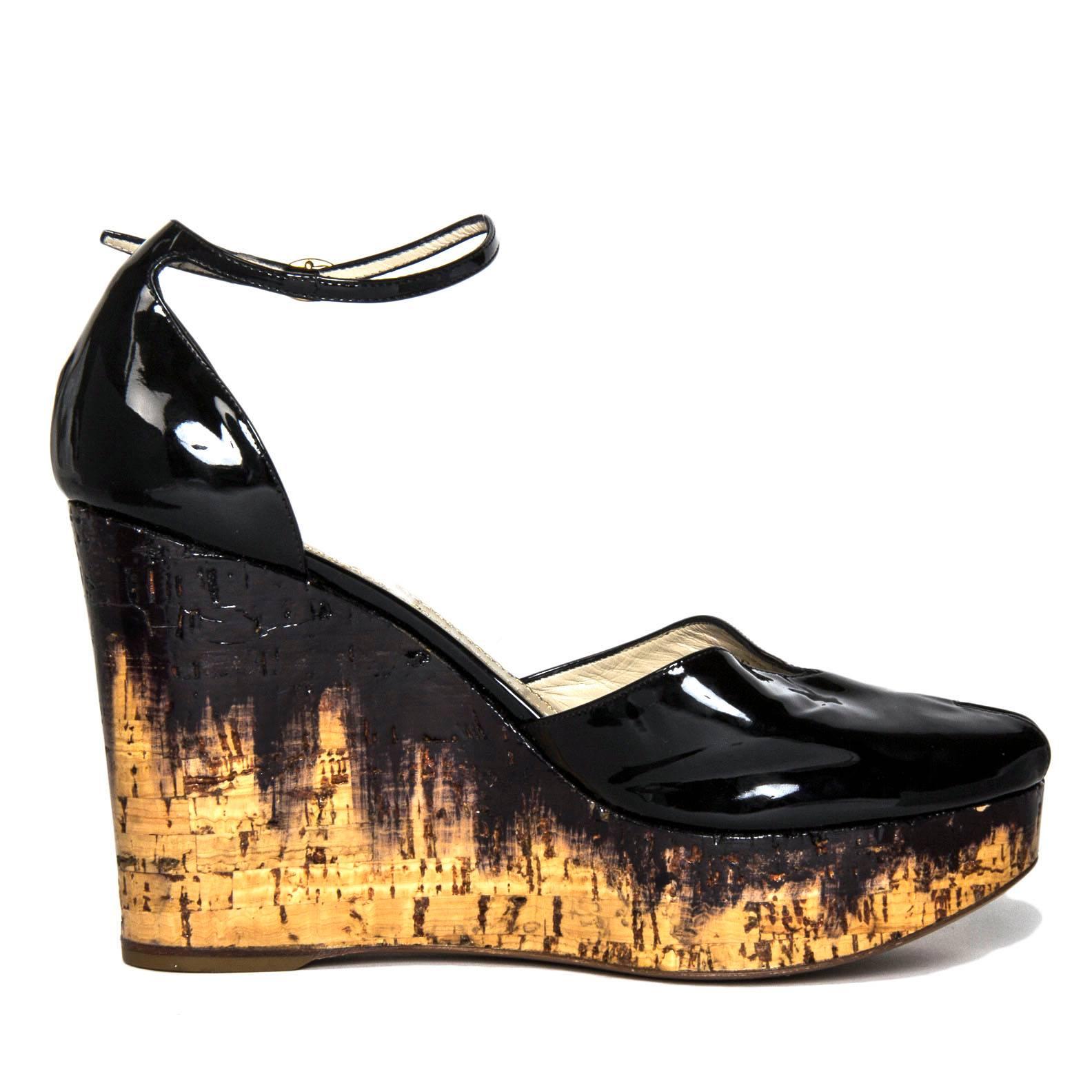 Black patent leather peep toe cork wedges with a thin strap at ankle that fastens with a little gold color buckle. The wedges are varnished to be shiny like the patent leather and brushed black paint seems to be dripping from the black leather. Made