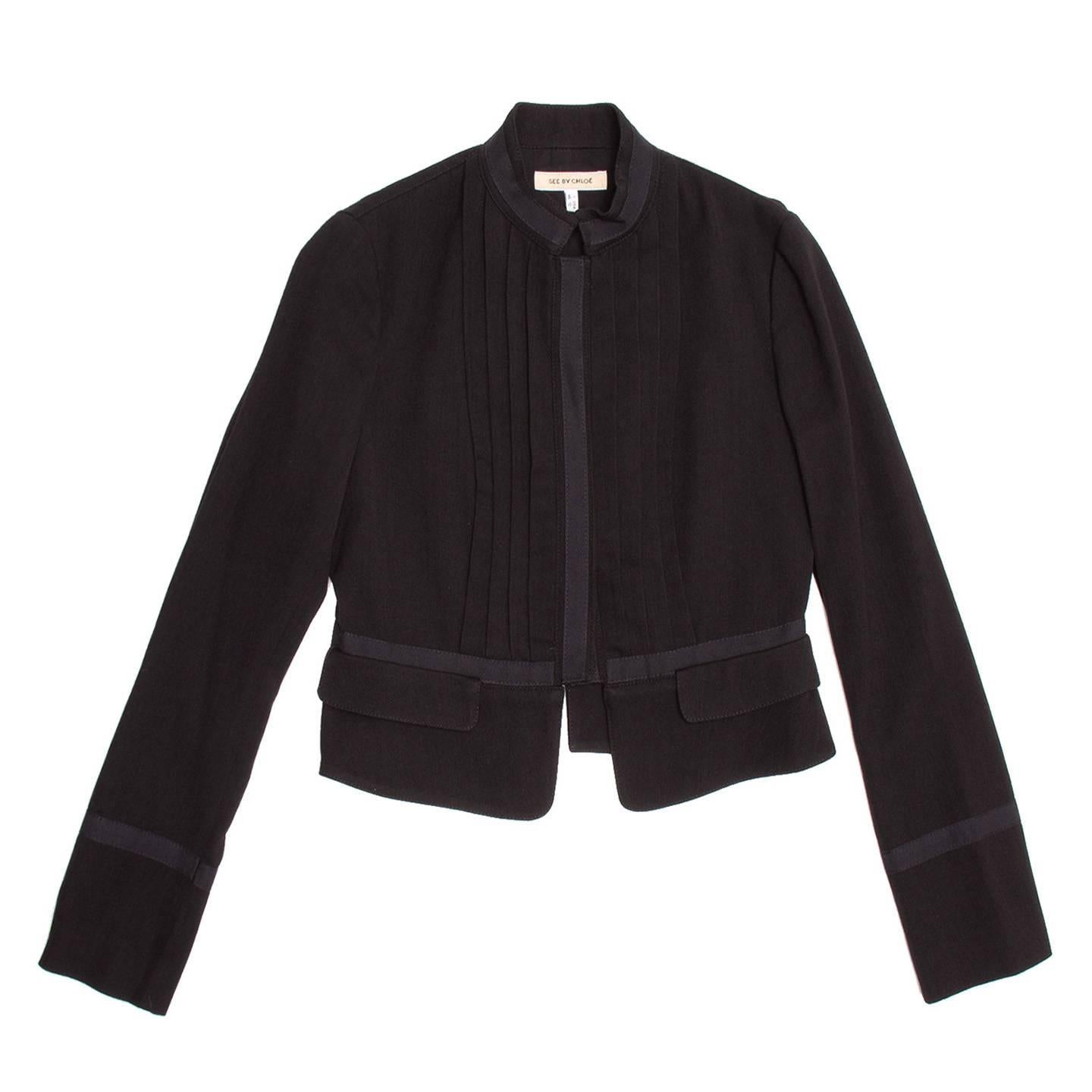 Black wool/cotton cropped bellboy style jacket with pleated front detail and tone-on-tone binding on neck, cuffs, waist line, front opening and back seams. The jacket fastens at center front with concealed metal snap buttons.

Size  46 Italian