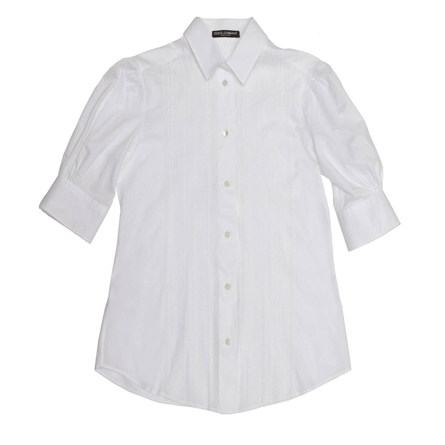 White cotton shirt with a front panel beautifully decorated by a fine cotton lace and a fix inverted pleat to enrich the center back. The body is quite shaped thanks to the back darts and the sleeves are short above elbow, slightly puffed and