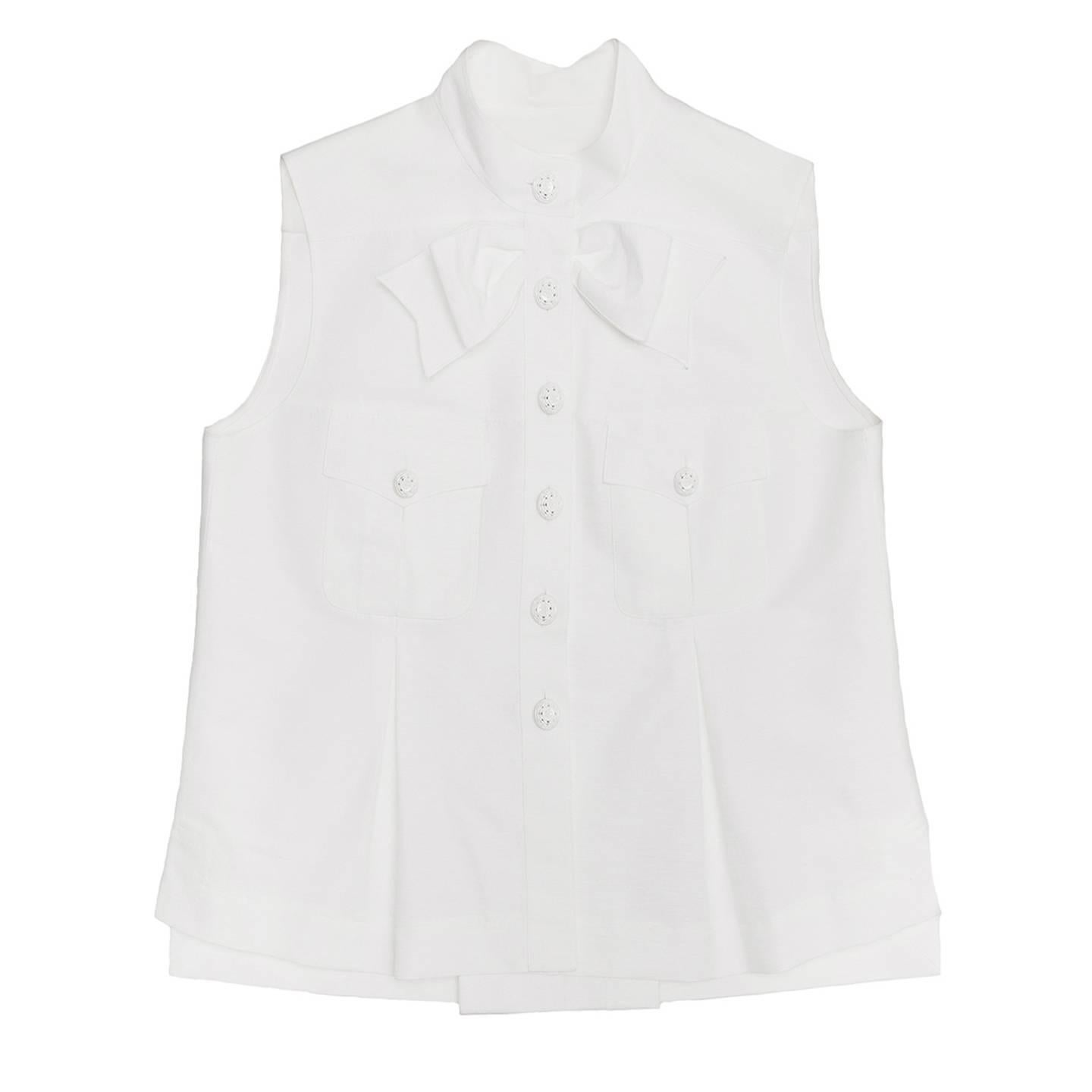 Elegant sleeveless ribbed white cotton blend shirt or jacket with nehru collar and white varnished metal flower buttons with Chanel logo embossed. The front is embellished by a large bow at under collar and bellow patch pockets with flaps fastened