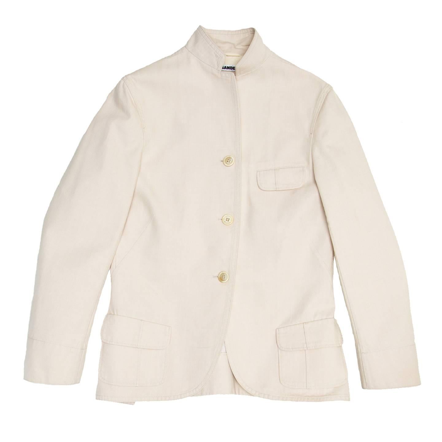 Ivory cotton jacket with a 3 button closure and small lapel. The blazer has a quite long casual style, with a little flap pocket at bust and slanted flap pockets on patch pockets at waist. The back vents are a continuation of the front darts, they