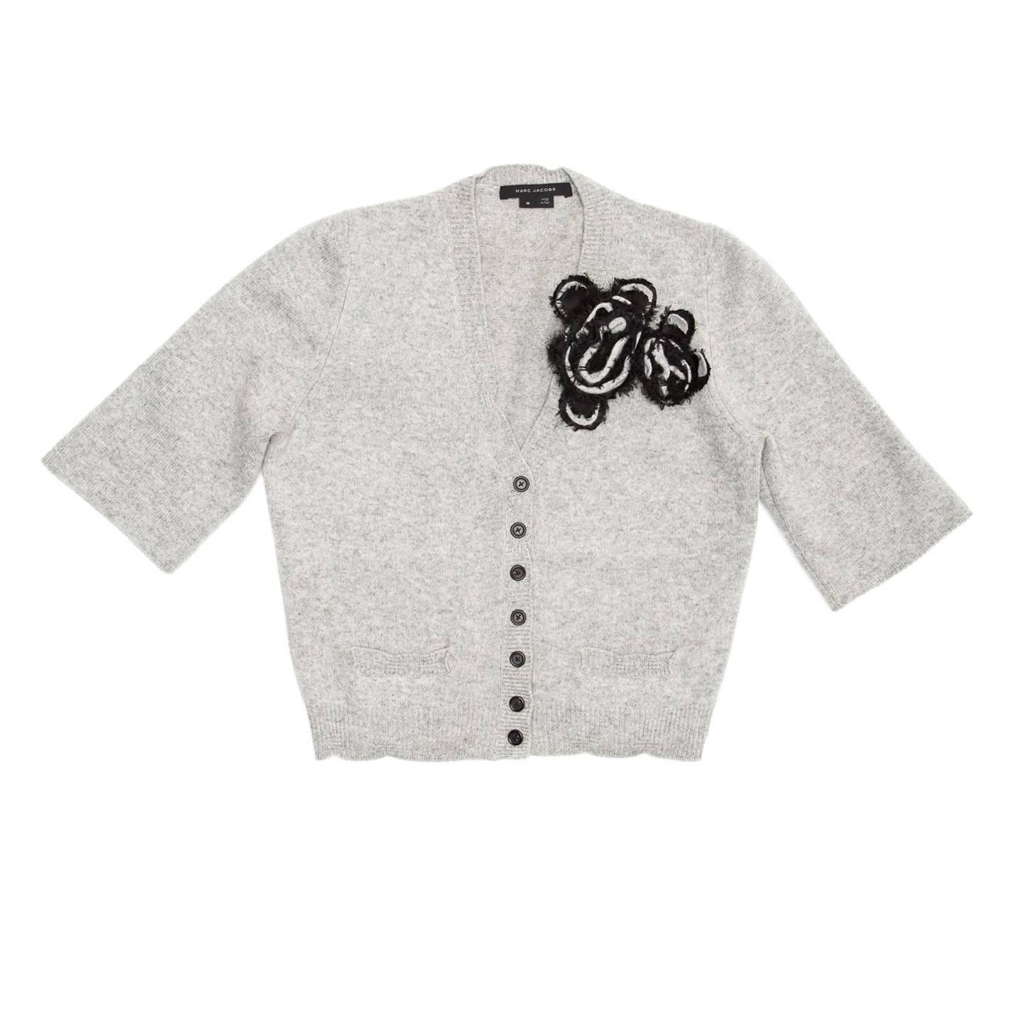 Light grey wool and cashmere knit cardigan with grey and black flower detail on the V-neck. The buttons at front are black to match the flowers, two little slit pockets sit near the hem and the 3/4 length sleeves are cuffless. All the ribbed parts