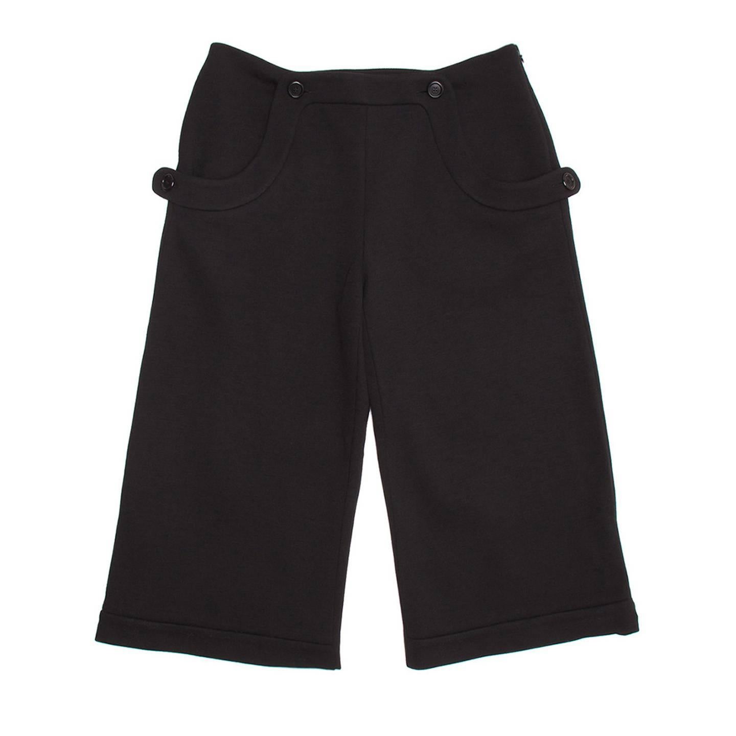 Black wool sailor style cropped culottes with broad hip pockets and side zipper opening. Wide self fabric binding detail at front waistline and scooped pockets with functional buttons. Back darts at back waistline and tab with button at back