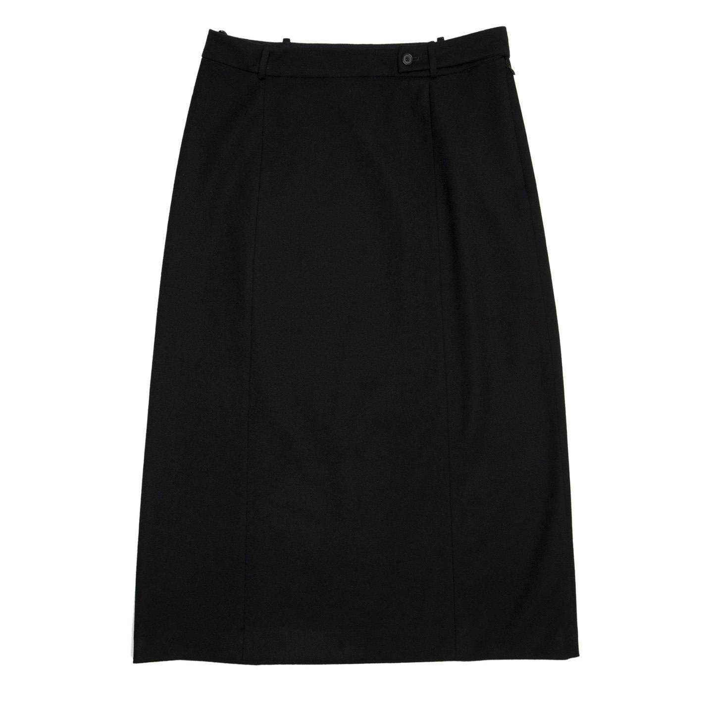 Prada Soft black wool straight knee length skirt divided in three panels at front and three panels at back. The waist band is longer on one side and it overlaps and fastens at front with a little button under one of the belt loops creating a nice