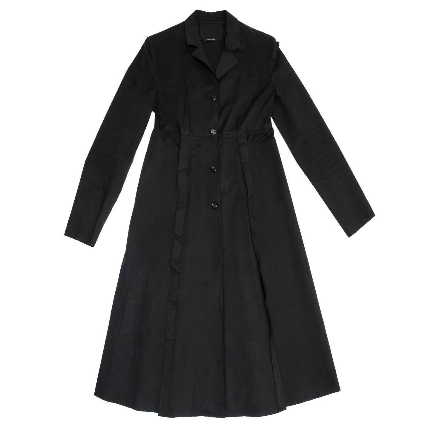 Prada black waxed cotton princess cut rain coat with narrow shoulders, empire line, flared hem, knee length and small lapel. A pleat enrich both back and front side seams creating a larger volume on skirt from below the princess cut. All the pleats