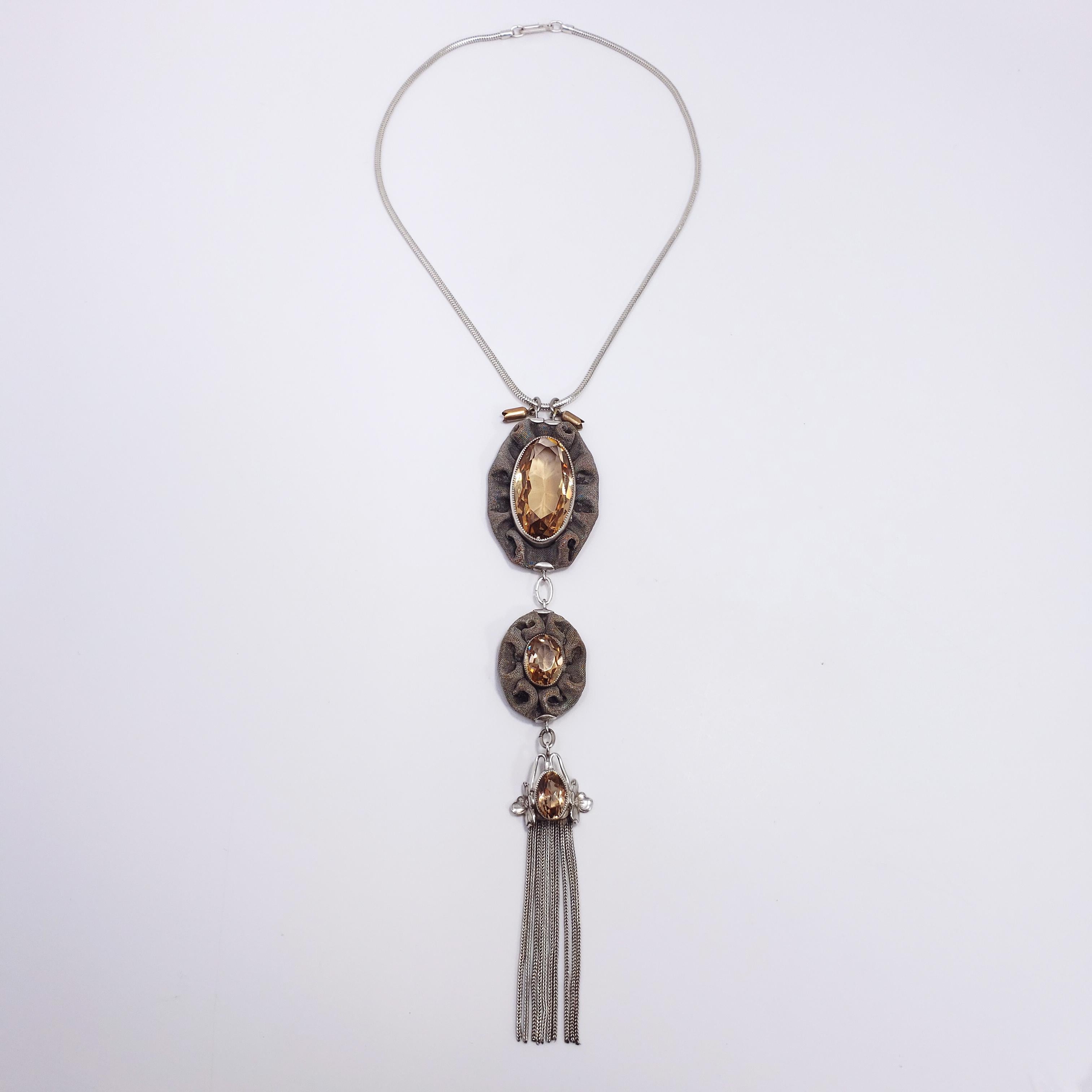 A handmade Victorian-era statement necklace. Three drop pendants hang in sequence on a snake chain. Each features an elongated, open back, champagne/topaz colored crystal set in a sawtooth bezel. Two of the pendants are set in a decorative sterling