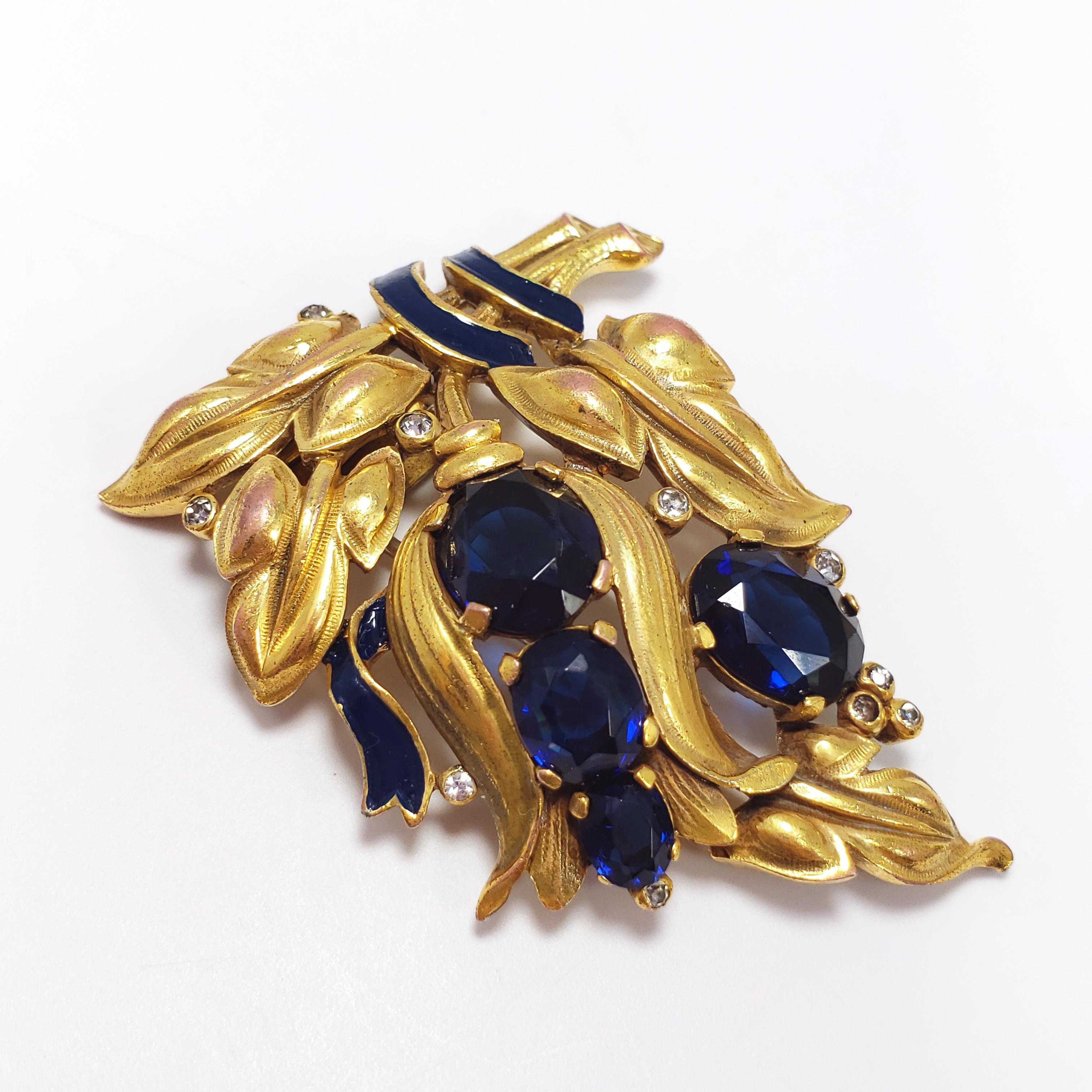 A vintage dress clip from Trifari (Crown), designed by Alfred Philippe during the mid 20th century. Features a gold-plated floral bouquet with prong-set sapphire-colored crystals, bezel set clear crystals, and blue enamel. A must-have for any