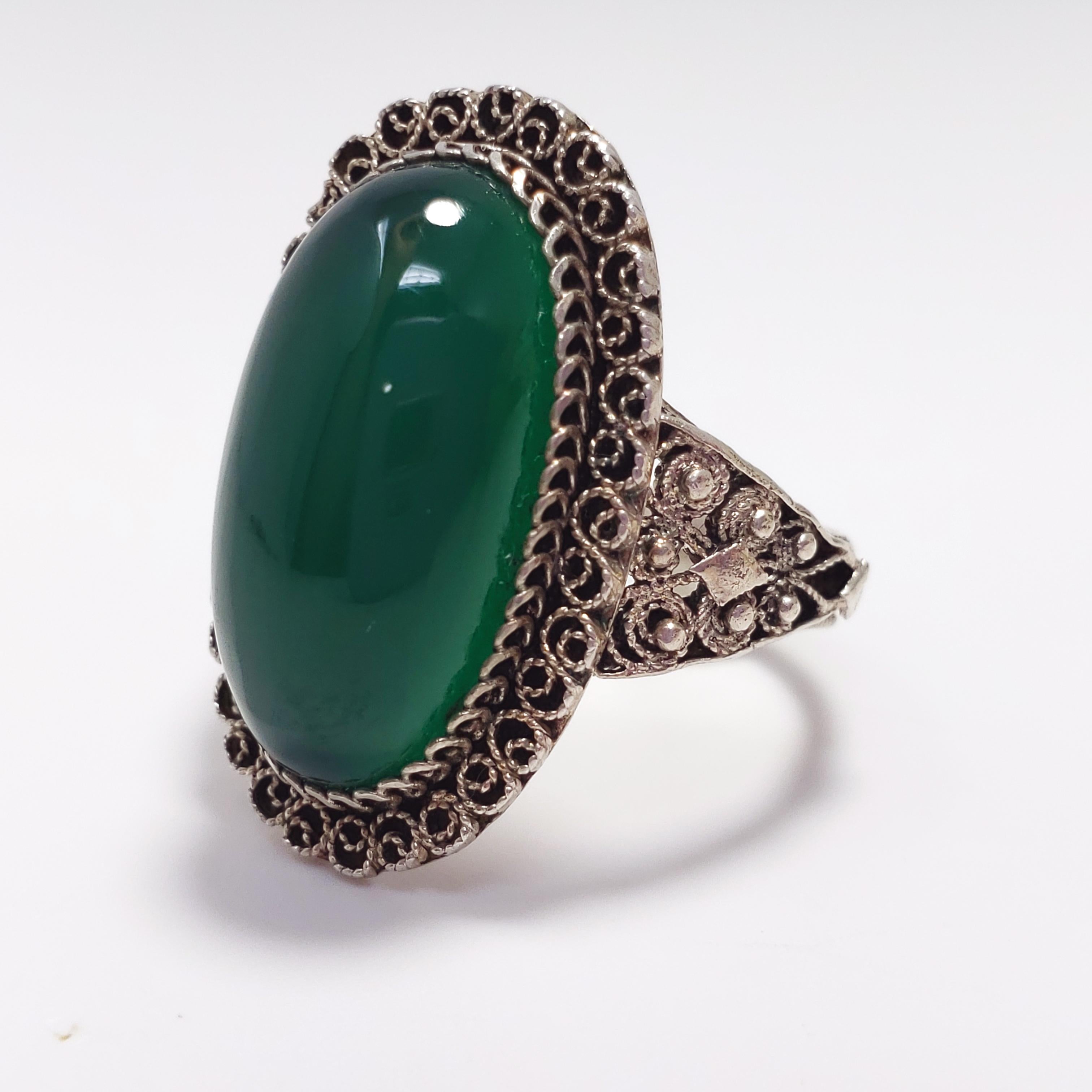 From the Victorian era, a decorative statement ring. Features a single translucent green art-glass cabochon set in .800 silver. The silver bezel and band have been accented with intricate detail, with no part of this ring left untouched! The perfect