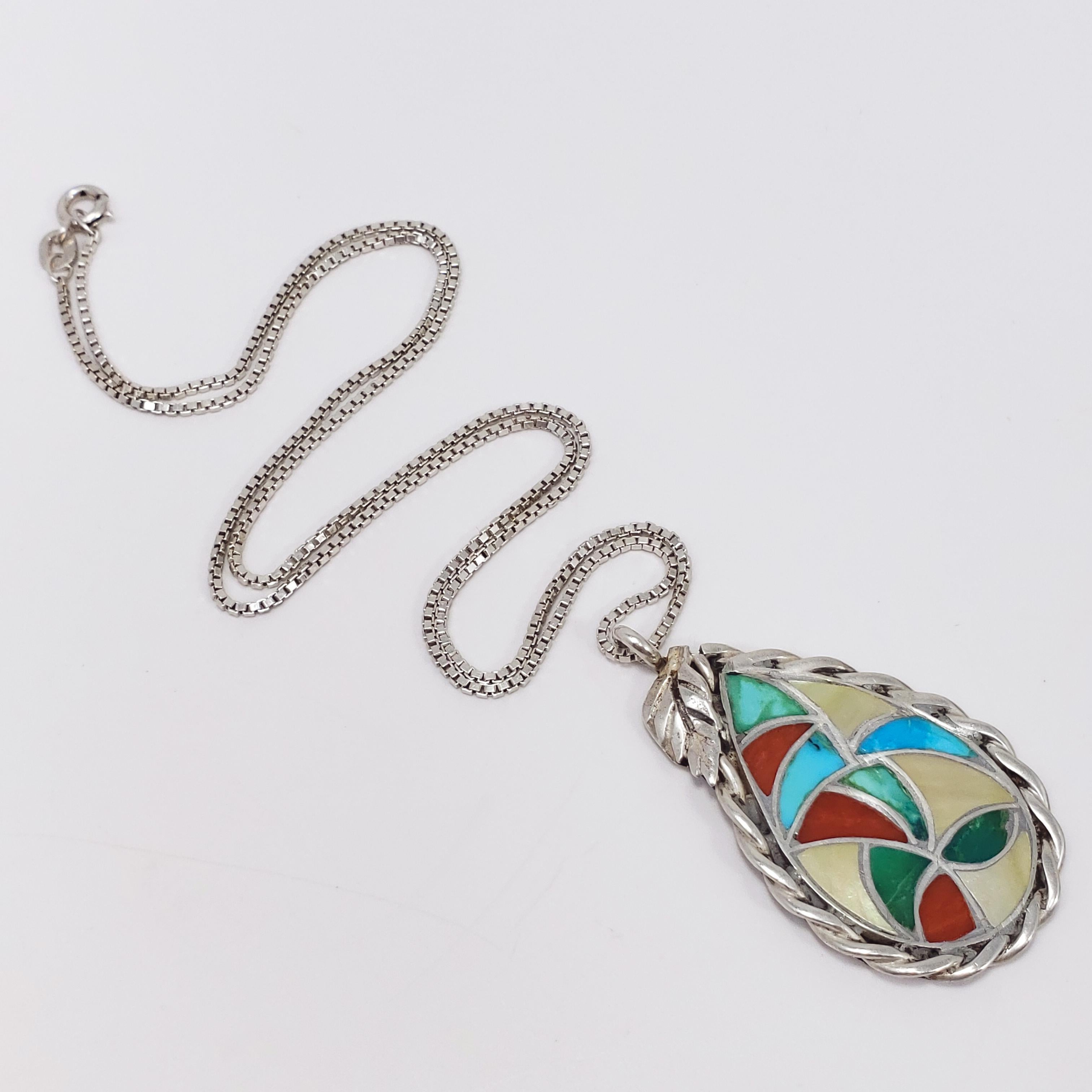 A colorful Native American Zuni pendant. Features coral, shell, and turquoise inlay in a tear-drop shaped sterling silver pendant. The weaved-strand bezel is accented with a single leaf on top. Comes with a complimentary matching sterling silver