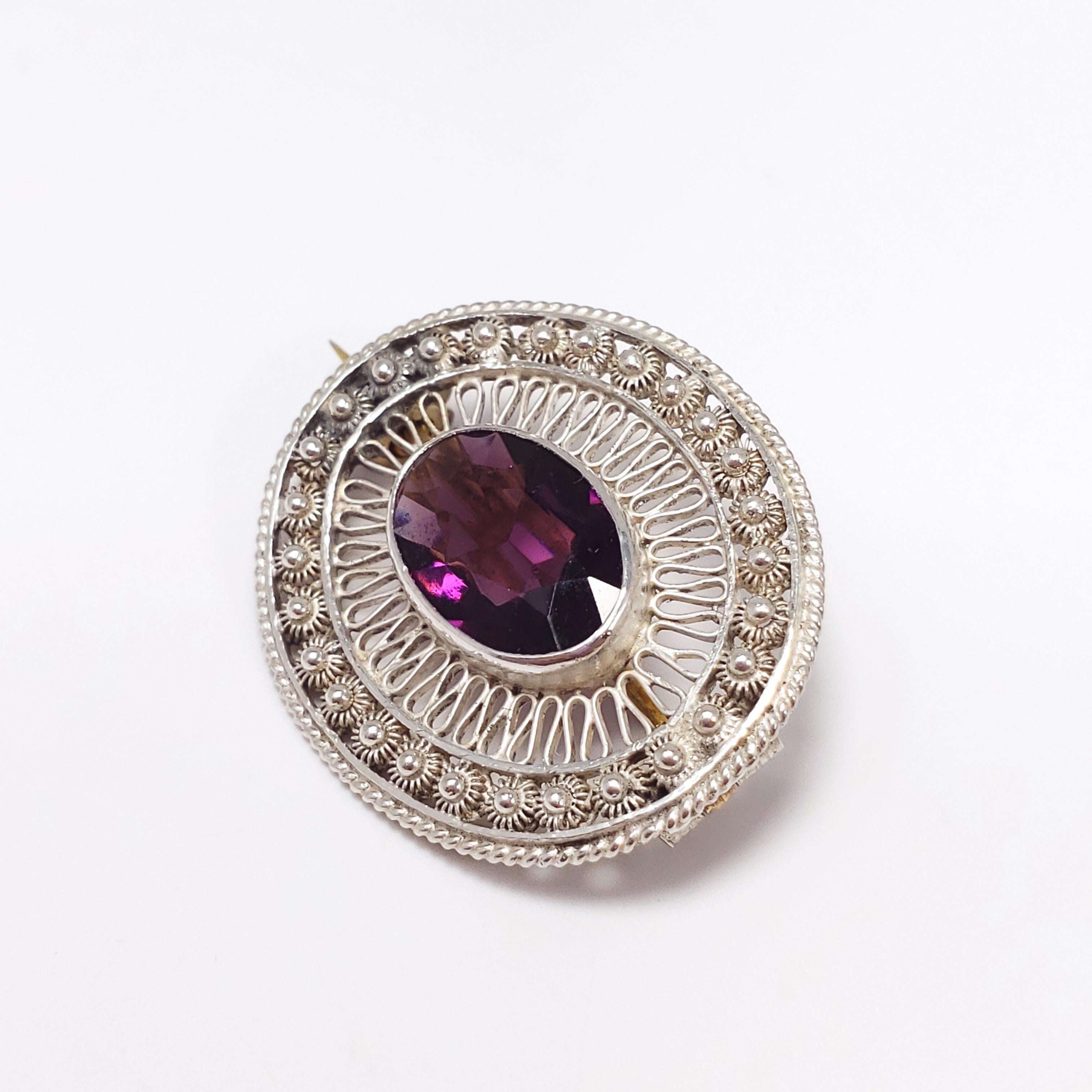 An amethyst open-back crystal sits in a meticulously designed sterling silver filigree-style setting, accented with decorative motifs. Features brass fastening hardware on the back. A gorgeous Victorian pin/brooch!

Dimensions: W 2.7 x L 2.2