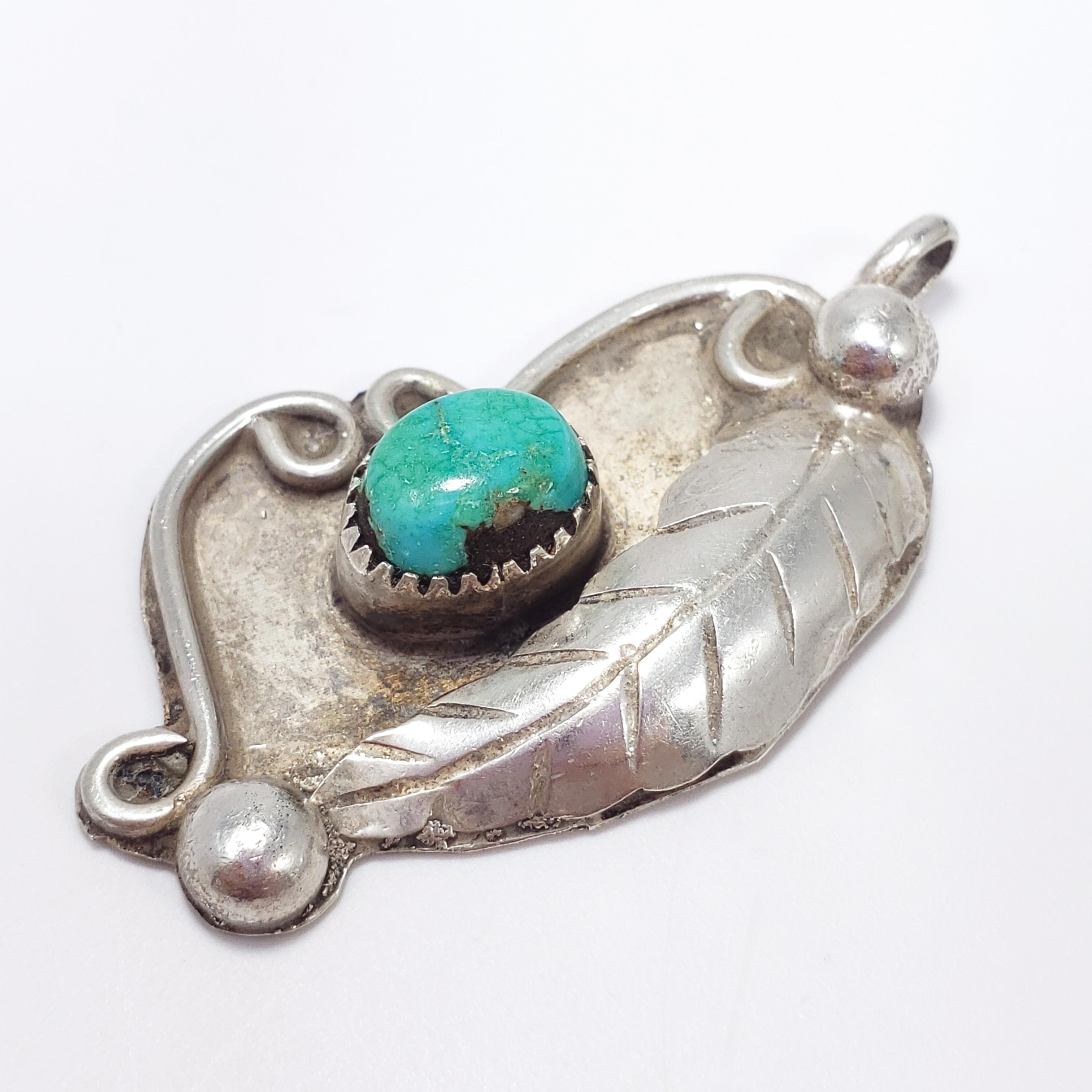 A handmade Navajo pendant featuring a decorative pendant, accented with a leaf motif and a genuine turquoise cabochon set in a sawtooth bezel. An authentic Native American accessory, circa mid 1900s.

Dimensions: L 4.1 x W 2.5 cm
Weight: 9 g
