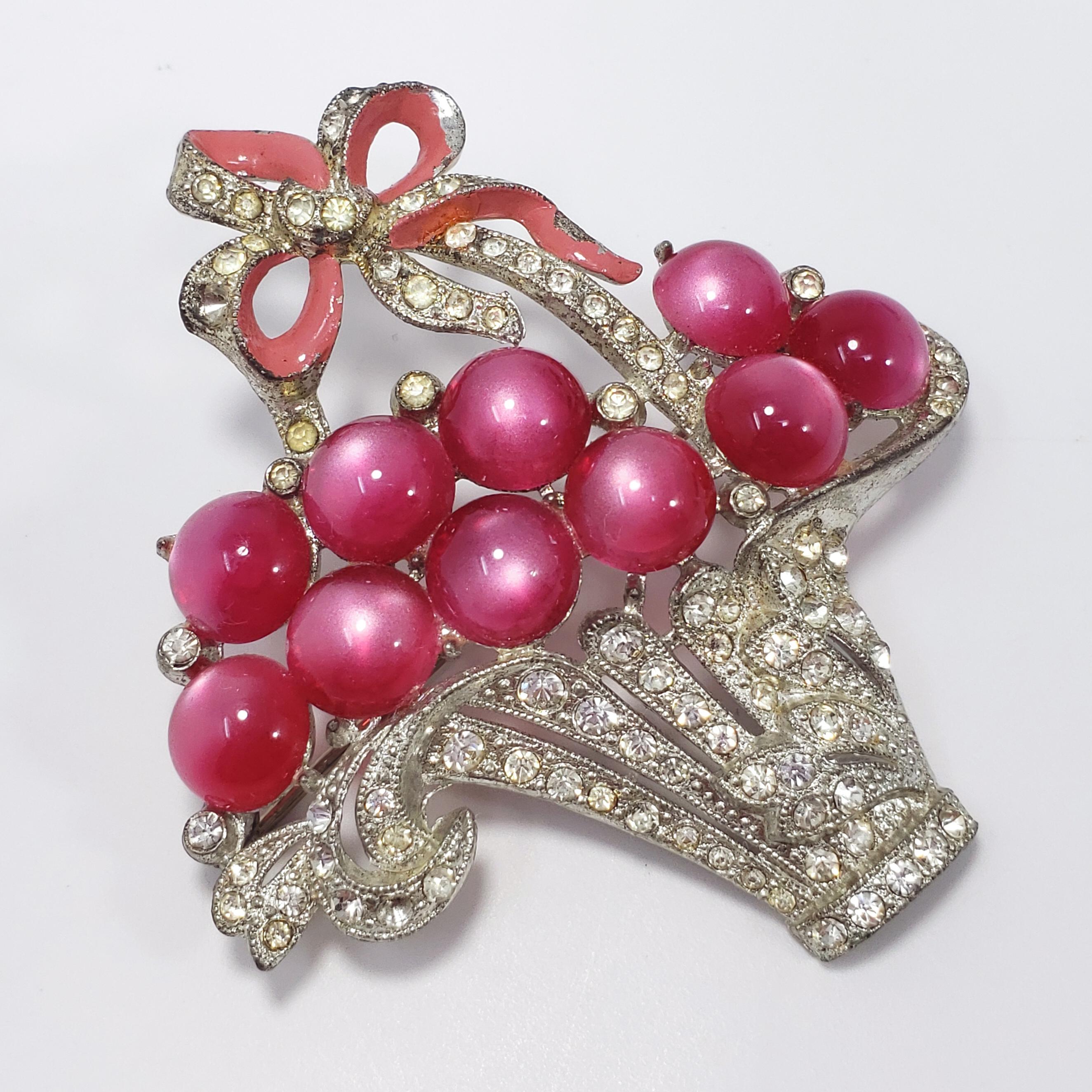 A vintage, circa mid 1900s fruit-basket themed pin/brooch. Features a crystal-encrusted basked filled with round violet moonglow cabochons. Accented with a light-pink enameled bow. Set on vintage pot-metal. A wonderful addition to your costume
