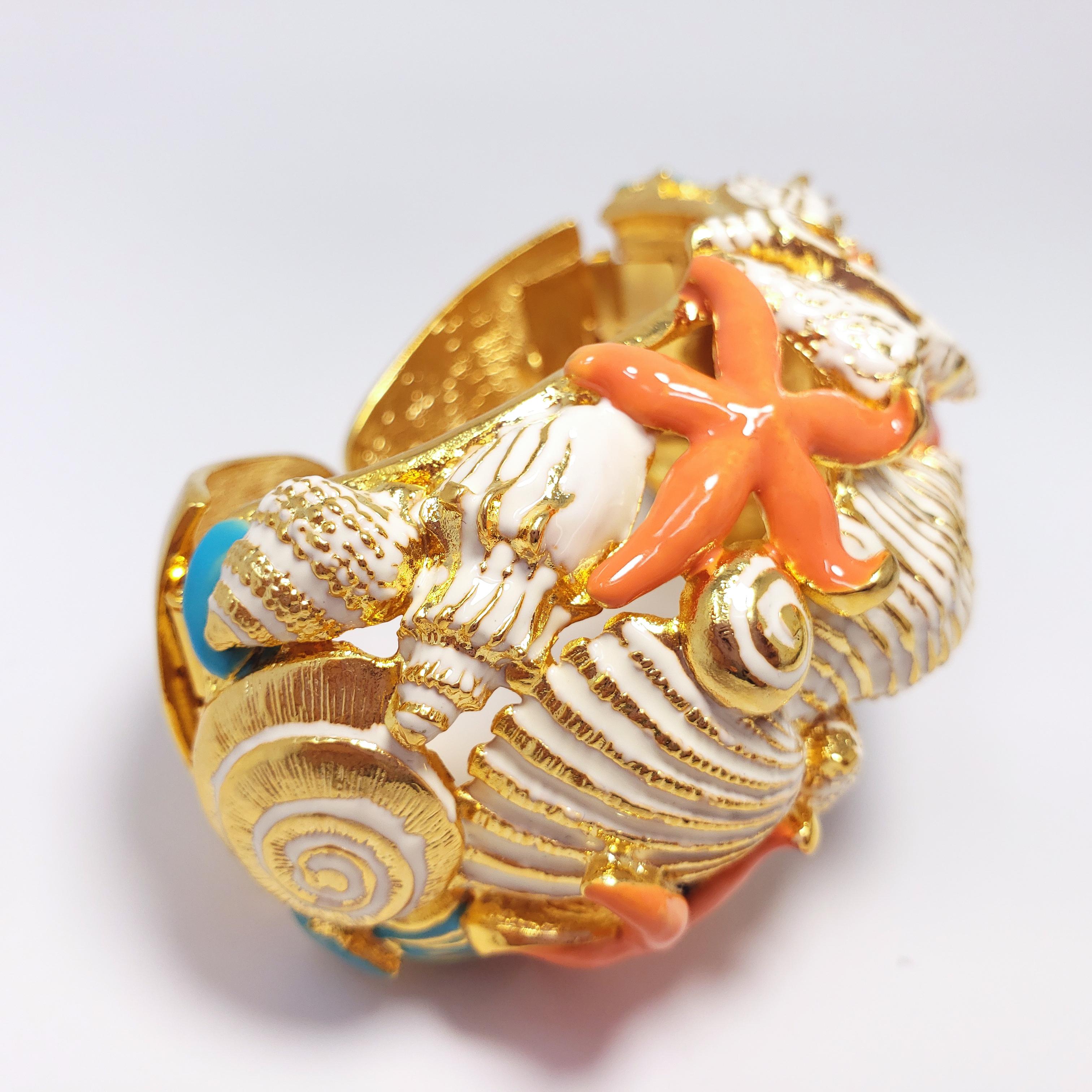 A colorful, nautical-themed cuff bracelet in Kenneth Jay Lane's traditional whimsical style. Features shells and starfish painted with white, turquoise, and coral enamel. Set in 22K gold plated, double hinged cuff.

Dimensions: 16 cm inner
