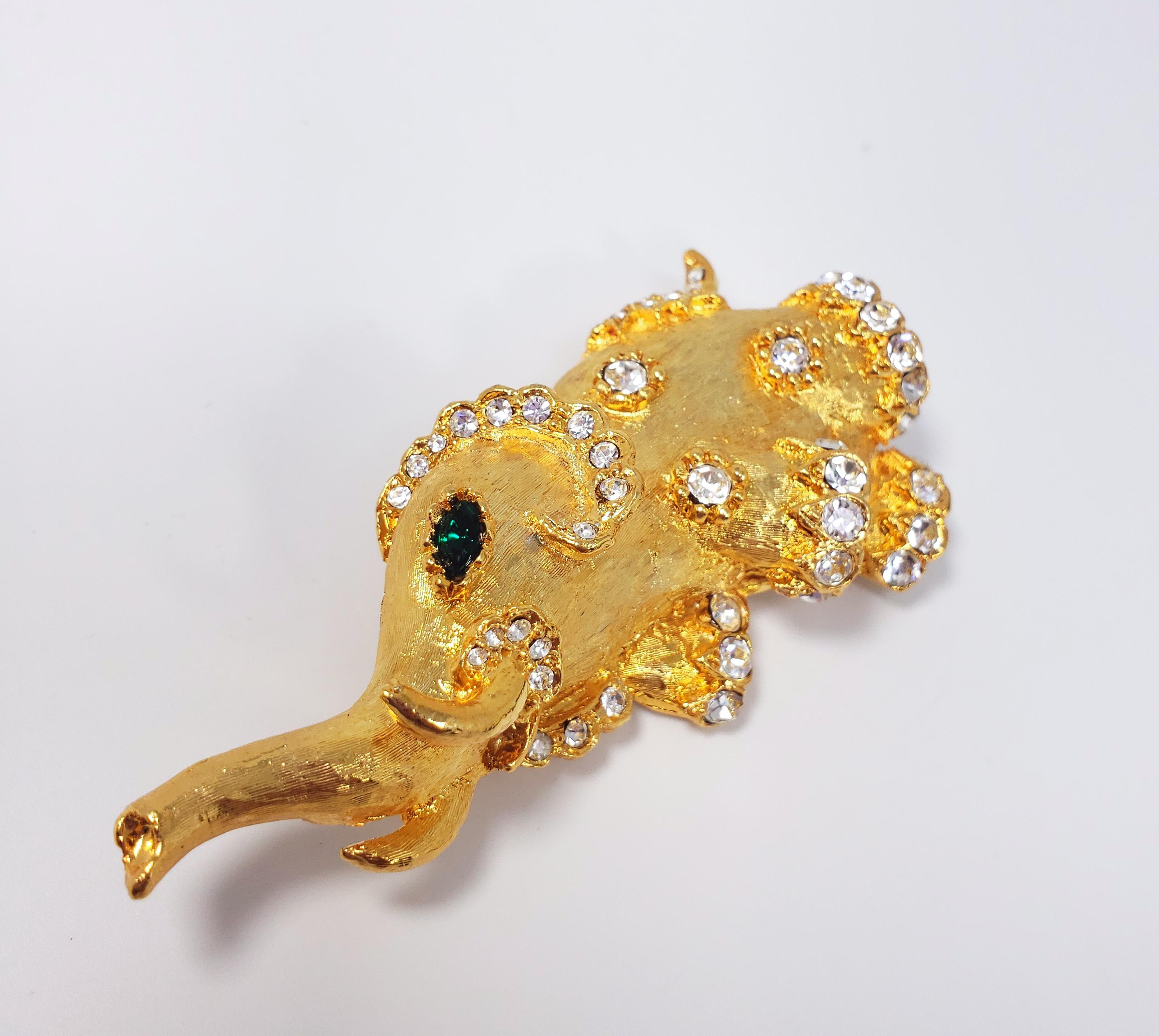 Cette broche excentrique de Kenneth Jay Lane représente un éléphant texturé en plaqué or jaune, avec deux yeux en cristal émeraude et des accents en cristal clair, le tout serti dans des billes décoratives. Fermeture par épingle de sûreté.

Poinçons