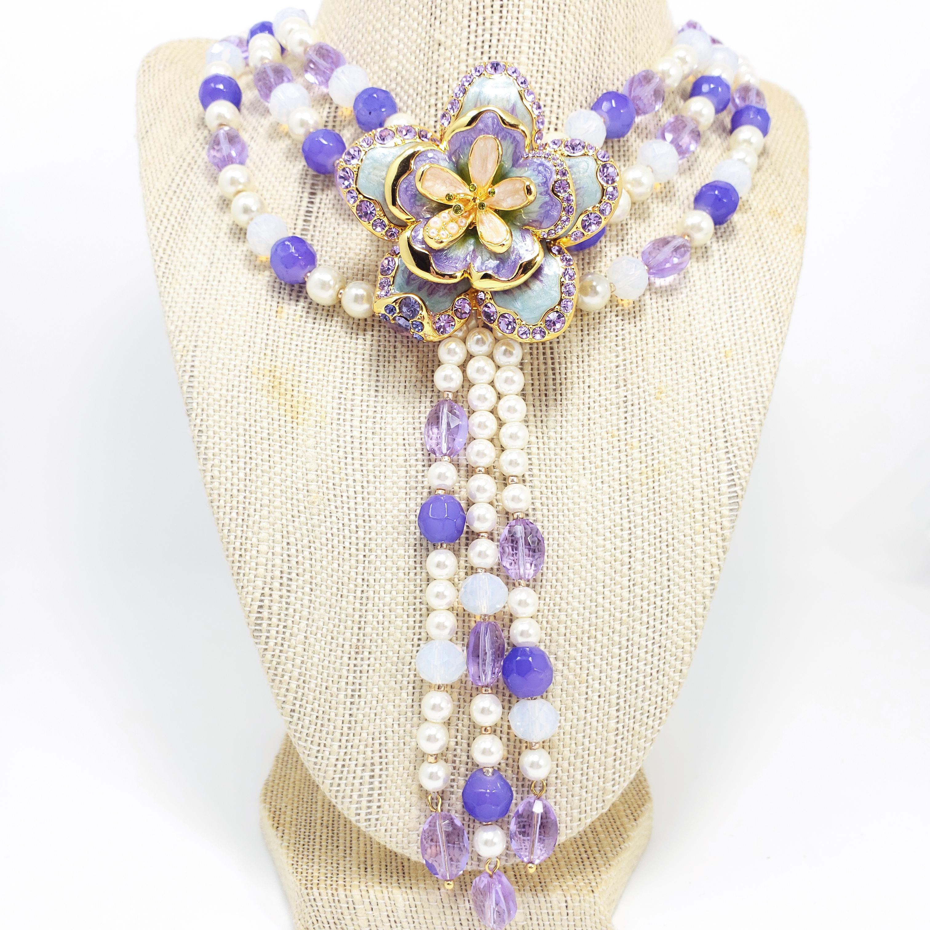 A triple-strand necklace featuring simulated pearls and faceted crystals in blue and lavender tones. Features a removable flower pendant, decorated with enamel, crystals, and simulated pearls on three dangling strands.

Jay by Jay Strongwater line,