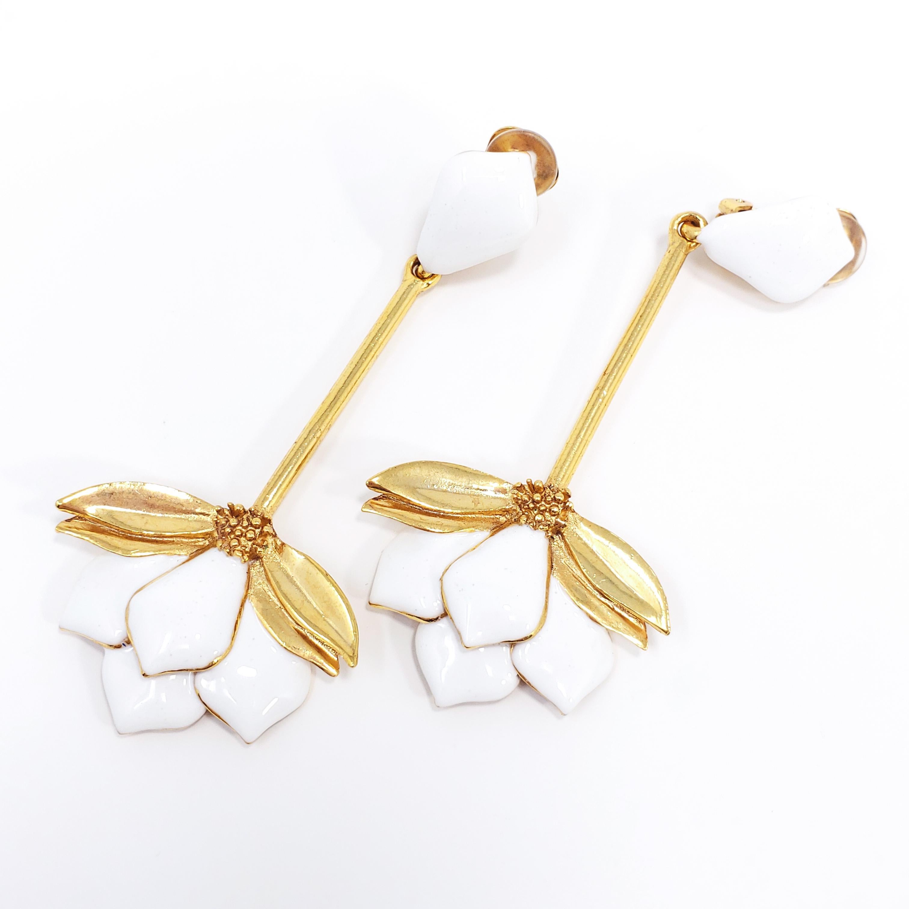 A pair of extravagant earrings, each featuring a clip on in white enamel, with a dangling long stem and gold plated, white-enameled flower, accented with golden floral motifs.

Hallmarks: Oscar de la Renta, Made in USA