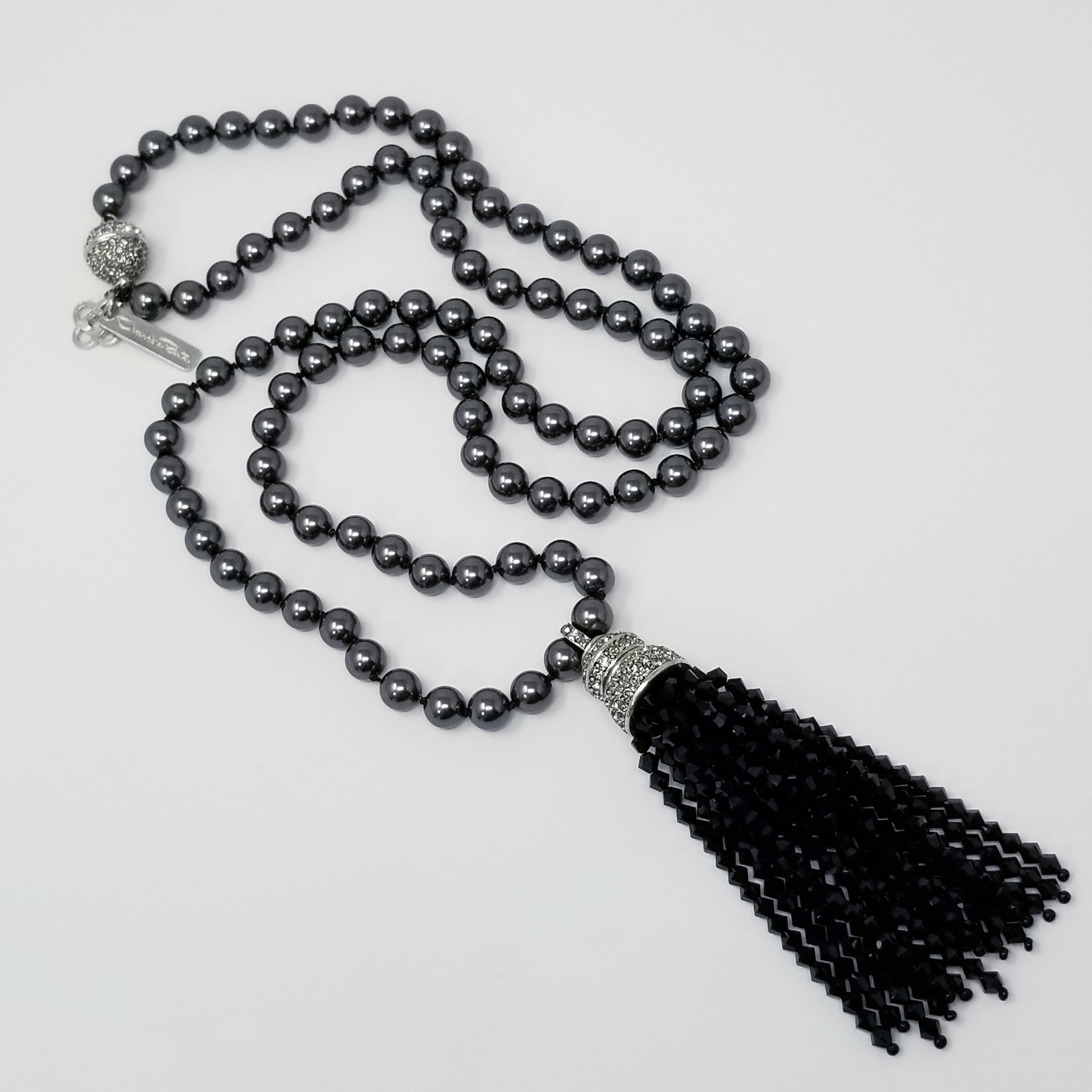 A chic bead necklace, featuring dark gray, metallic, reflective beads on a knotted string. The tassel features a rhodium plated metal motif, encrusted with clear crystals and hanging black faceted crystal strands. Pave crystal ball closure. Radiates