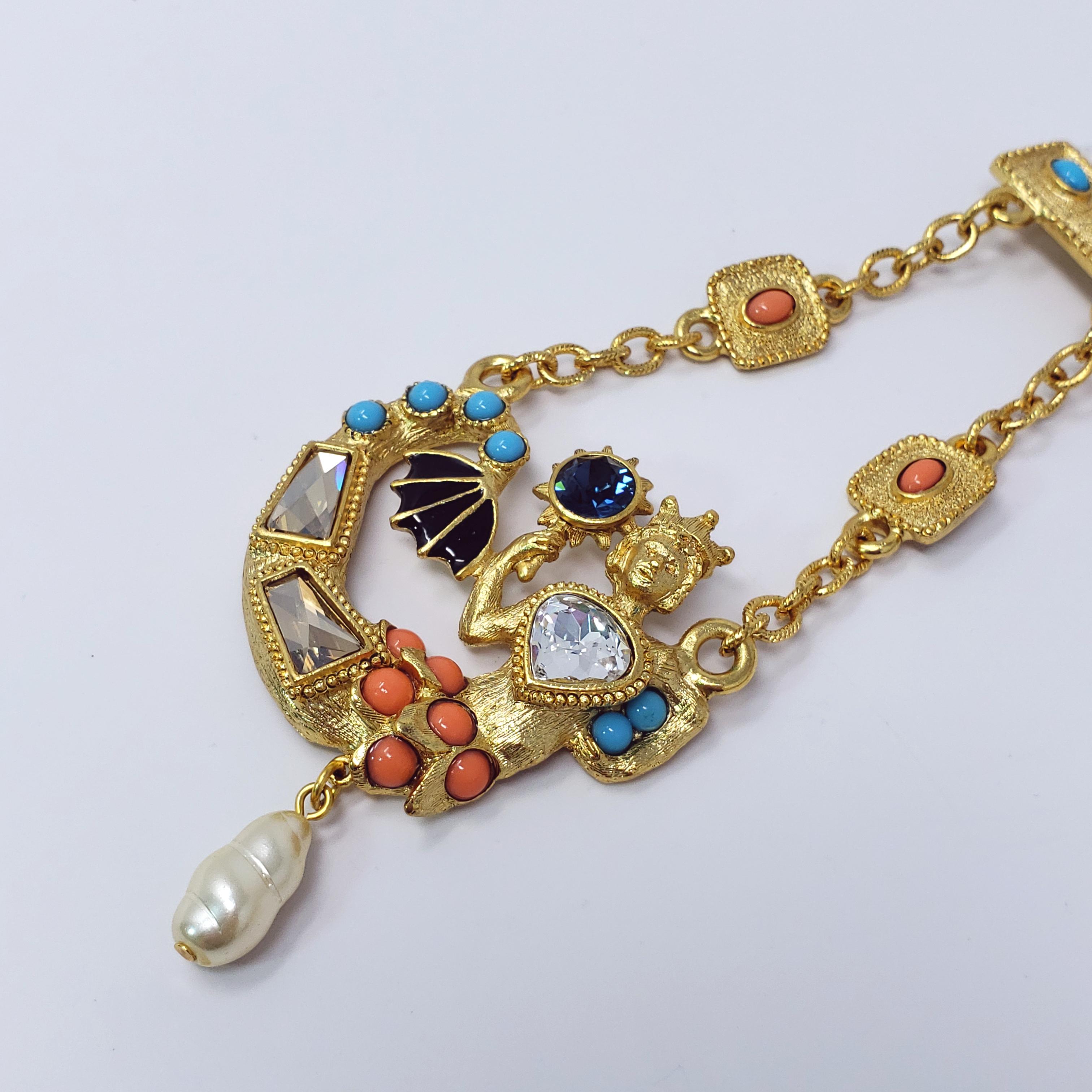 Renaissance-inspired mermaid brooch by designer Kenneth Jay Lane. Gold plated dangling mermaid accented with faceted clear, sapphire, and light topaz colored crystals, coral & turquoise colored cabochons, and black enamel. A single faux pearl hangs