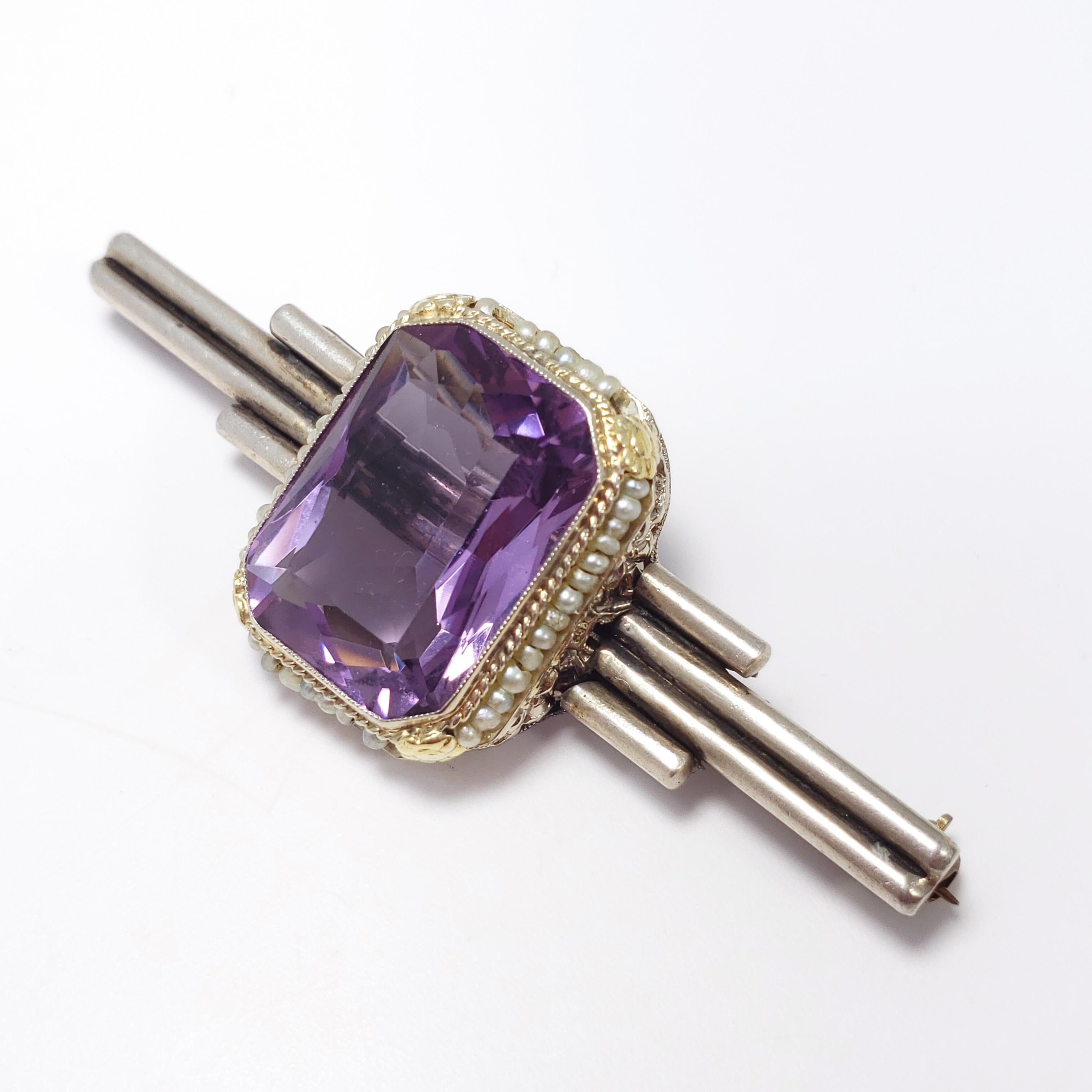 This Victorian art-deco brooch features a 1.8 x 1.4 cm centerpiece faceted, open back amethyst gemstone, surrounded by real seeded pearls and set in a gold-plated sterling silver filigree and floral motif bezel. The bezel sits on an art-deco