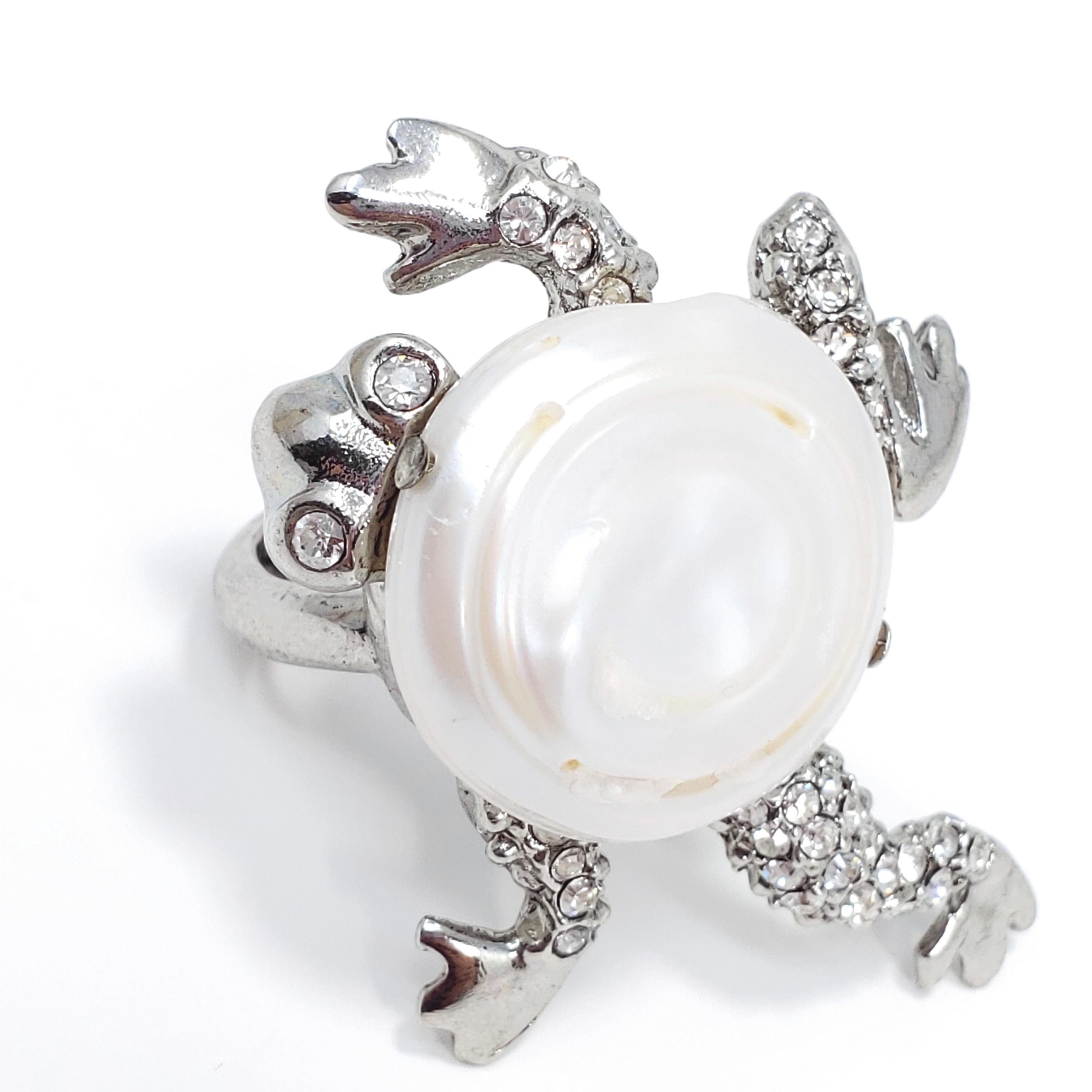 Quirky, yet elegant, frog motif ring by Oscar de la Renta. Features a genuine mother of pearl center, accented with clear pave crystals. Rhodium plated metal setting.

Hallmarks: Oscar de la Renta, Made in USA
Size: US 4-8, adjustable
Frog motif