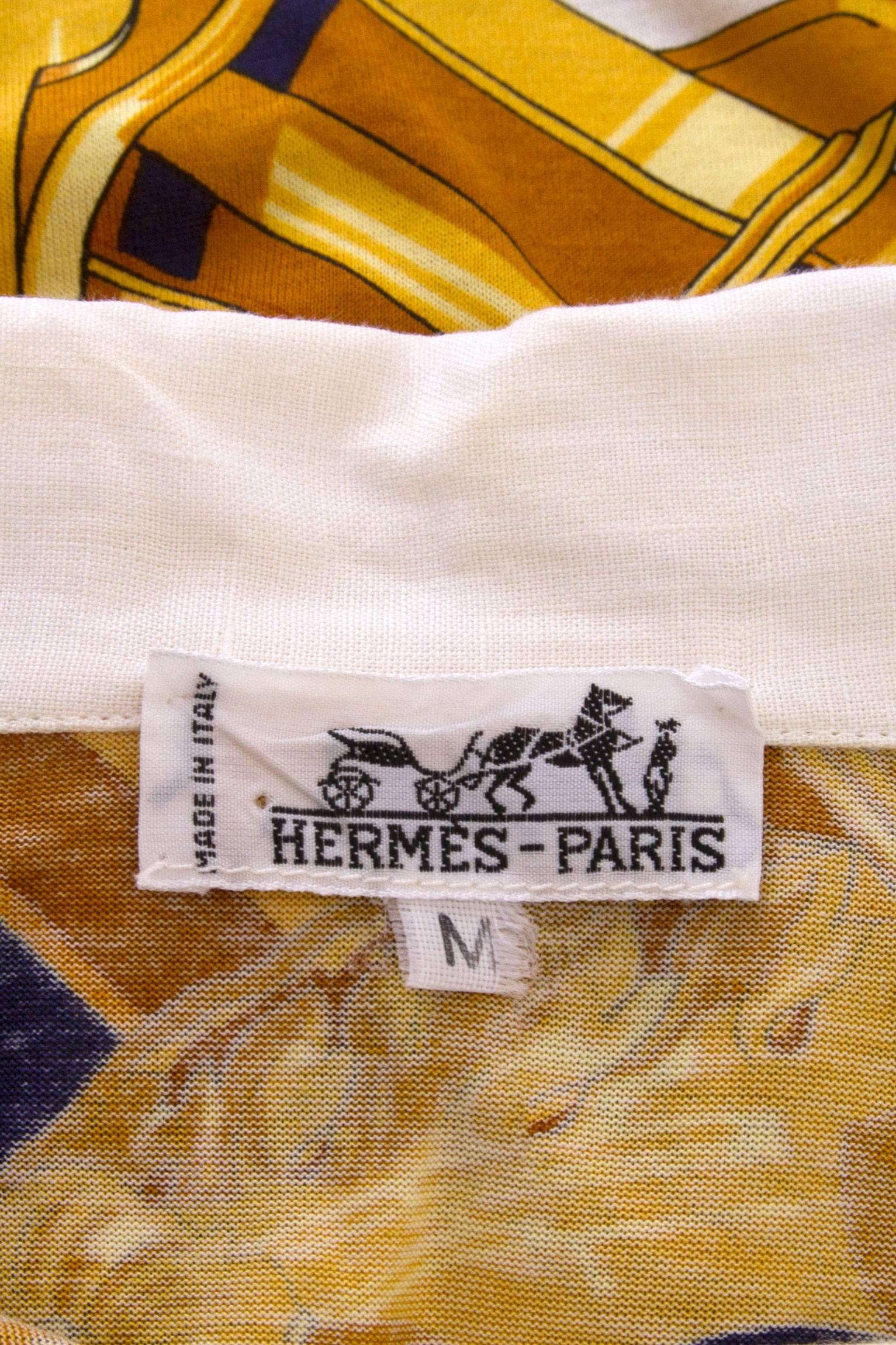 A 1980s printed Hermès cotton t-shirt with a contrasting white button up collar and short sleeves. The intricate print is held in bright yellow and navy tones, whilst a contrasting printed trim runs along the hem. The title ‘Rythmes’ is printed on