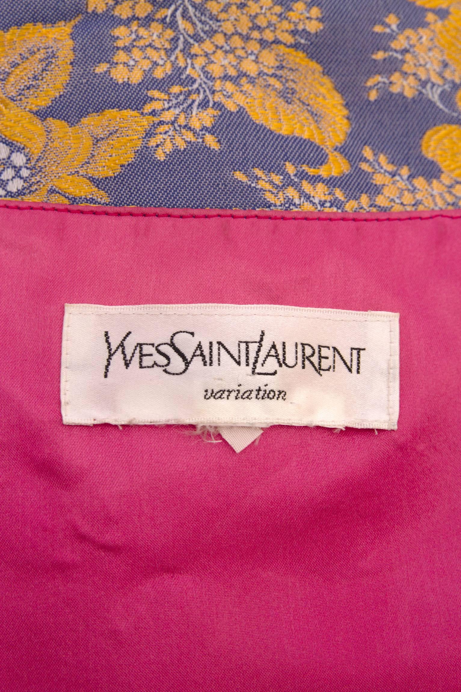 A gorgeous 1980s Yves Saint Laurent open brocade vest in purple and gold. The cropped waistcoat has a row of large gold buttons on each side of the open front. All the buttons are embellished with a large rhinestone setting. The vest is fully lined