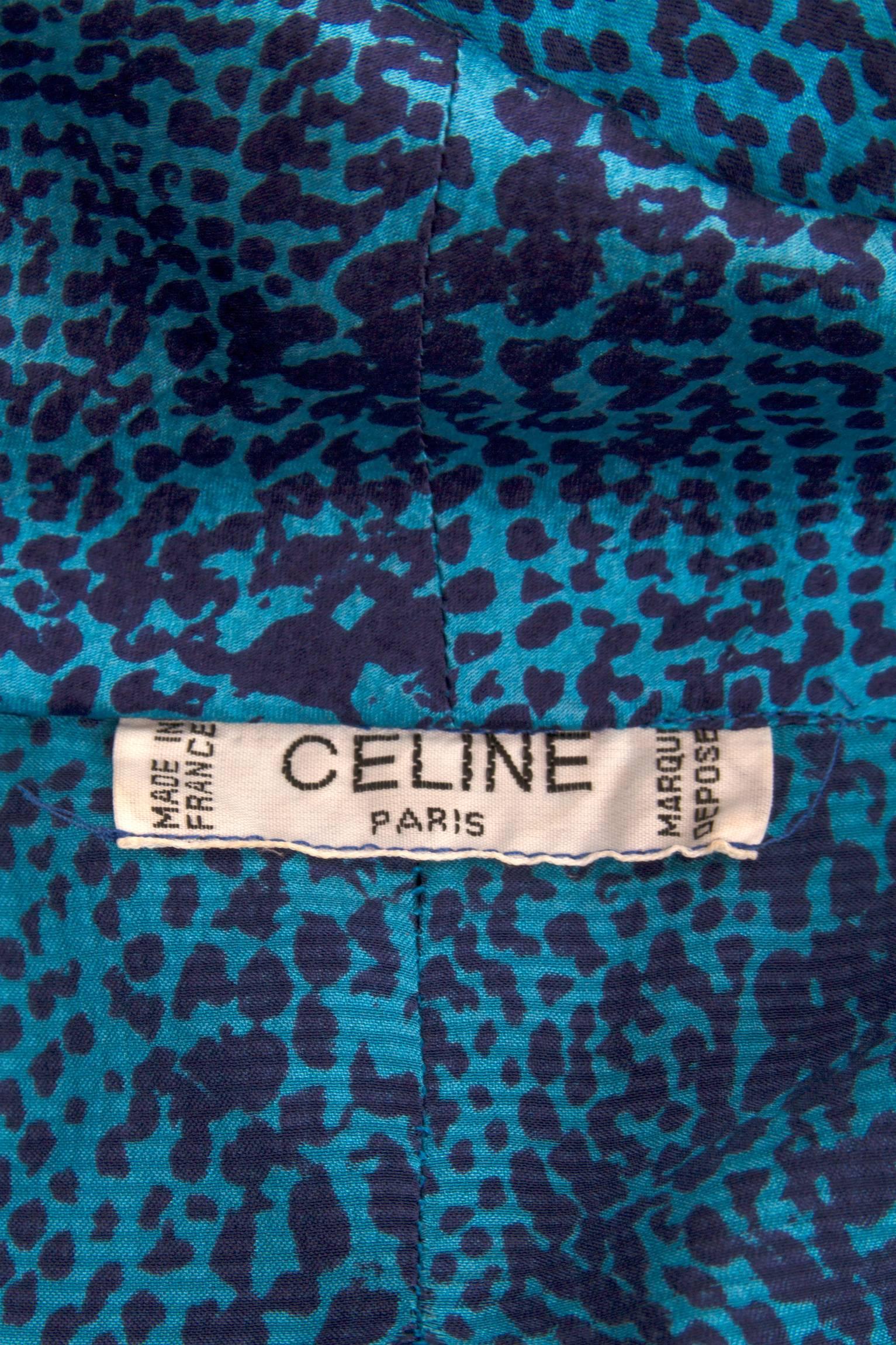 A 1980s Celine blue silk dress with black python print and a voluptuous asymmetrical pussy bow closure at the neck. The bow covers an asymmetrical row of hidden but matching blue logo engraved buttons. The dress has one buttoned cuffs and a slit at