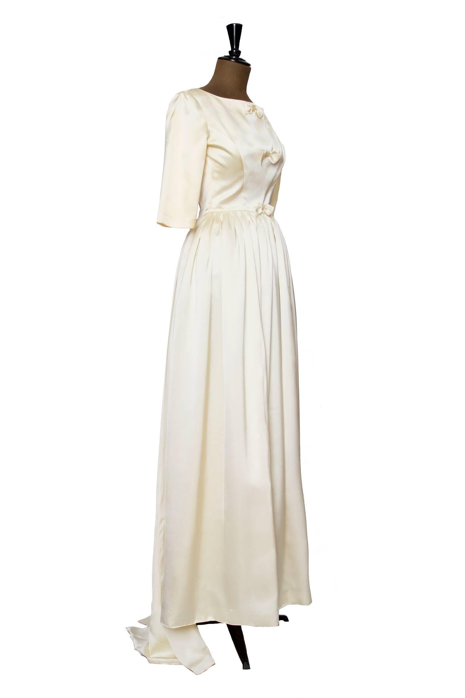 A gorgeous 1960s Maggy Rouff heavy silk wedding gown with a full floor length skirts and three quarter length sleeves. The structured bodice is embellished with a vertical row of three identical bows. On the back a 130 cm split train elegantly falls