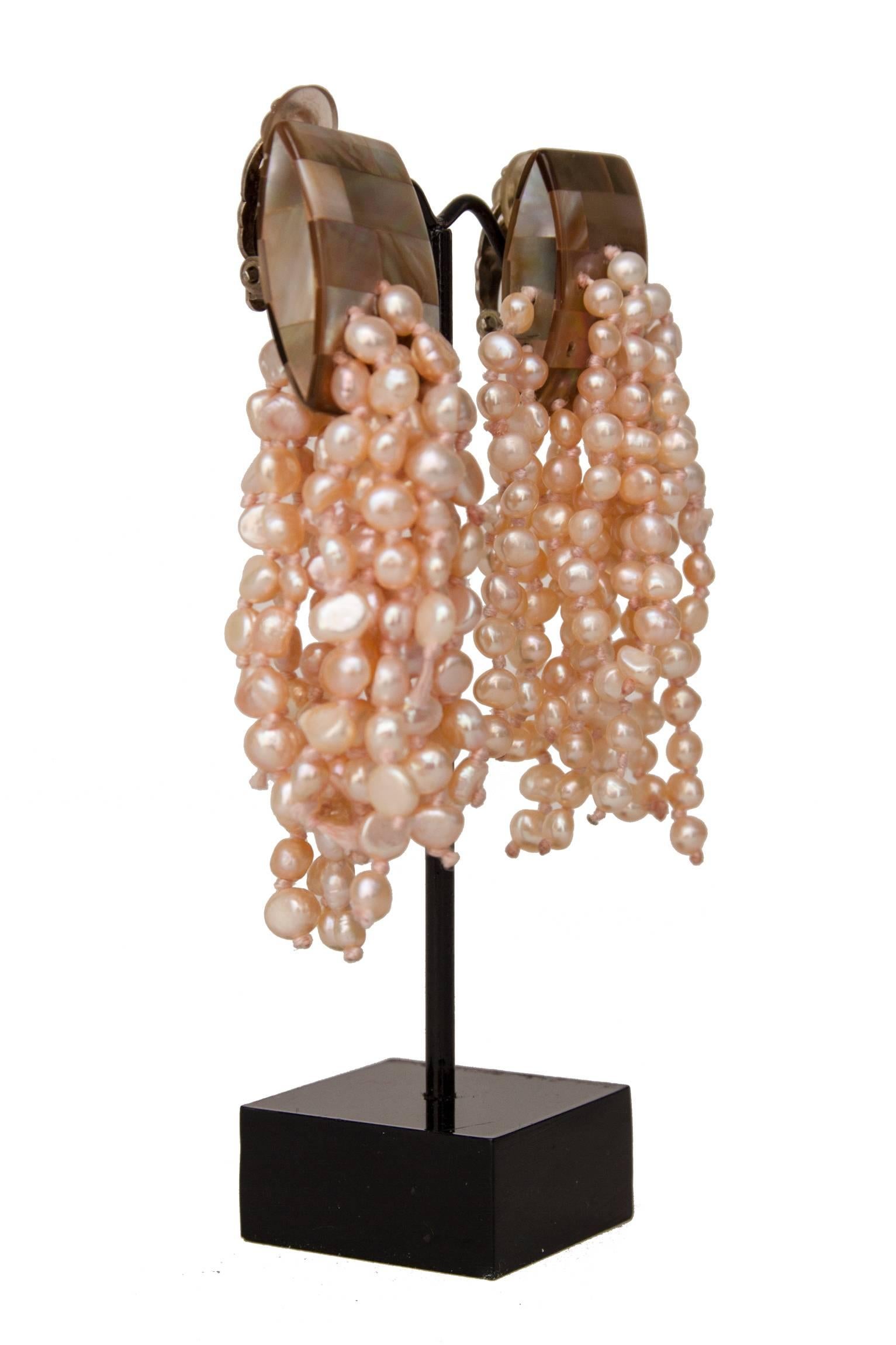 A pair of 1980s pale-pink Monies mother-of-pearl dangle clip-on earrings with a mosaic-like top and different strands of pearls attached to each earring.

The earrings are stamped: Monies 