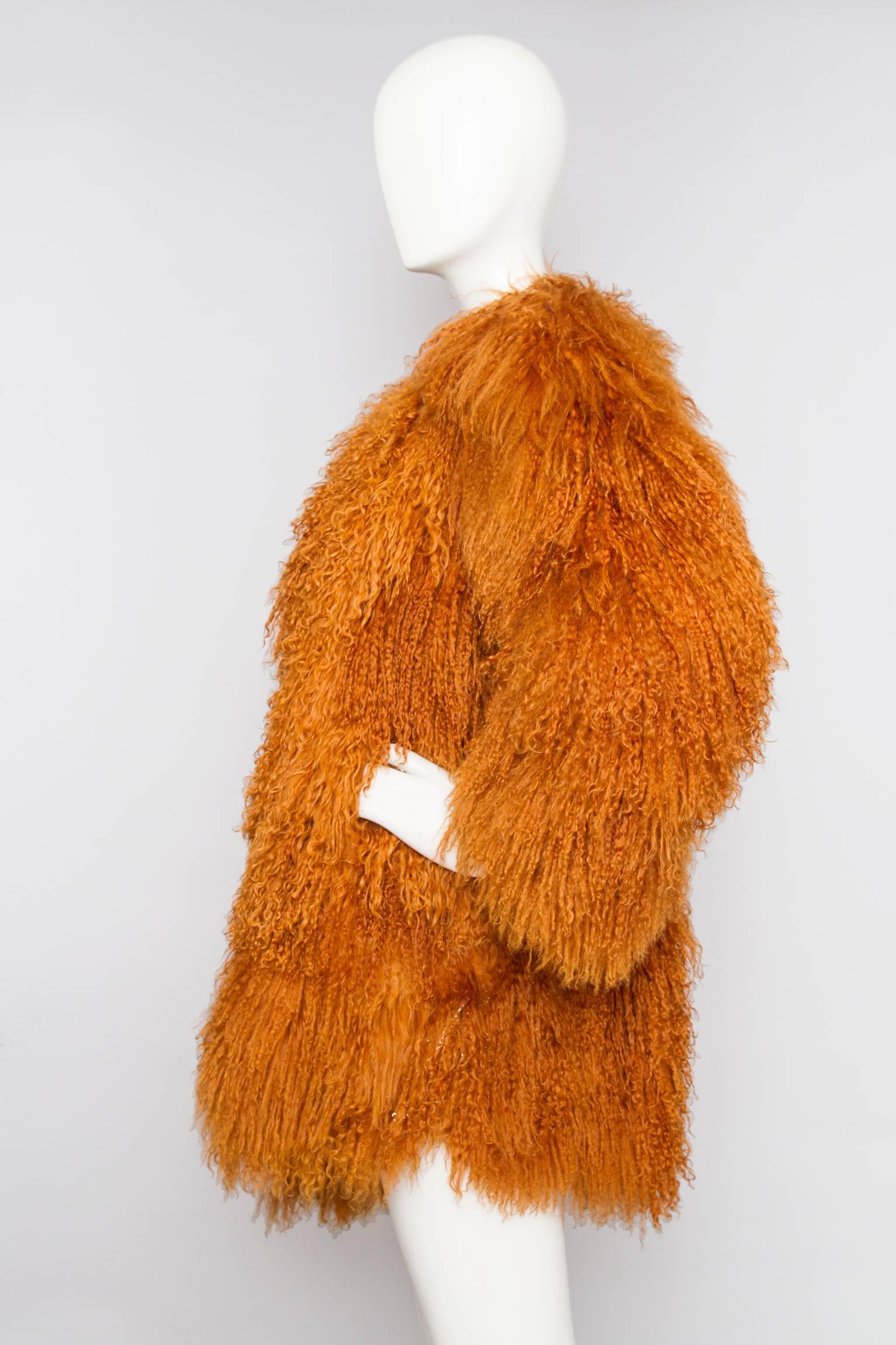 A stunning 1990s Yves Saint Laurent orange Mongolian lamb fur coat with a round neckline and a front hook button closure. The glamorous coat has exaggerated shoulders, side pockets and is fully lined in matching brown silk with jacquard YSL logo