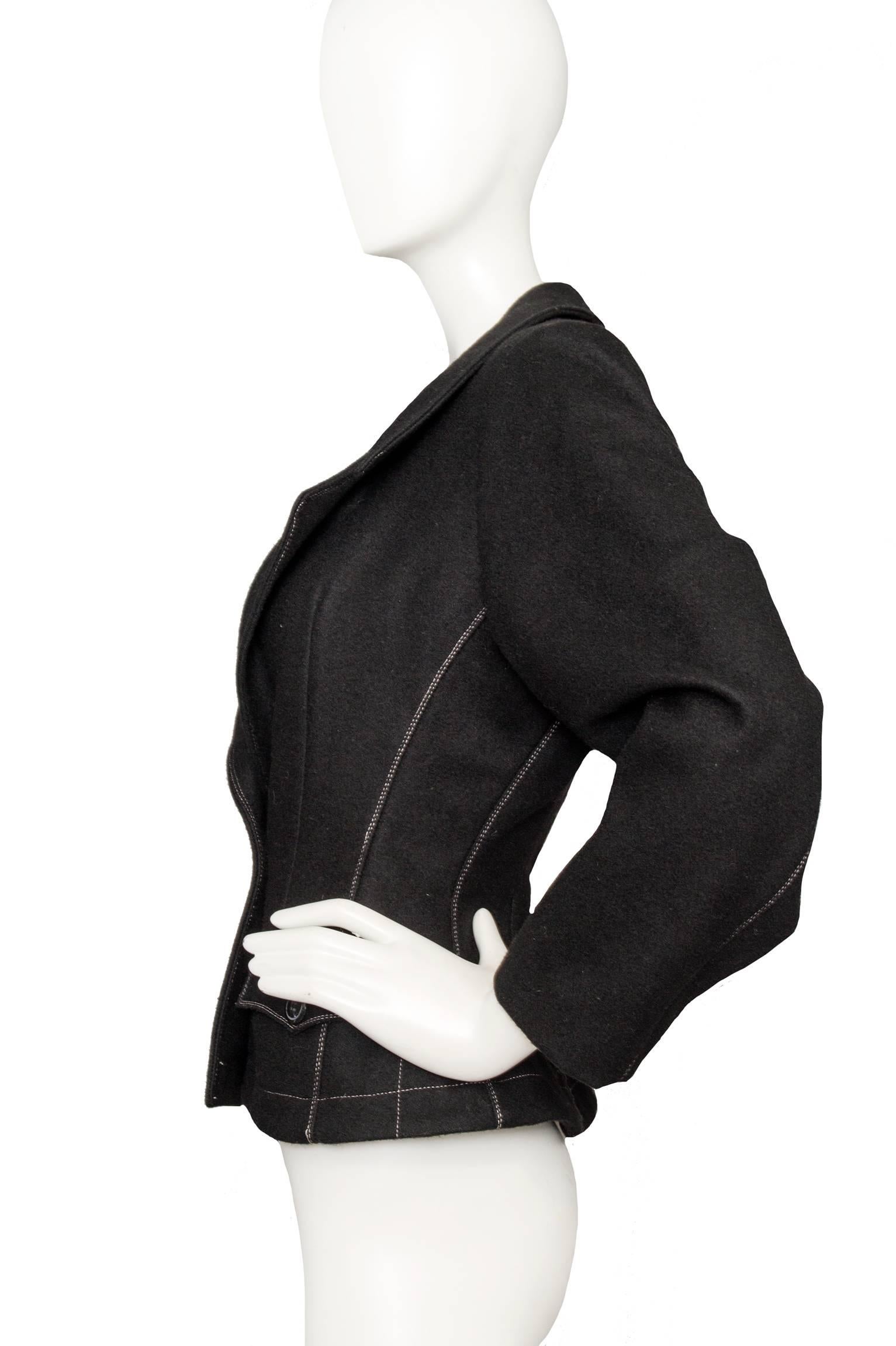 A modern 1990s black Gaultier Junior felt blazer with contrasting white stitching. The deep neckline is framed by slim lapels with rounded edges. The visible stitching follows the lines of the upper body and two front flap pockets. 

The size of