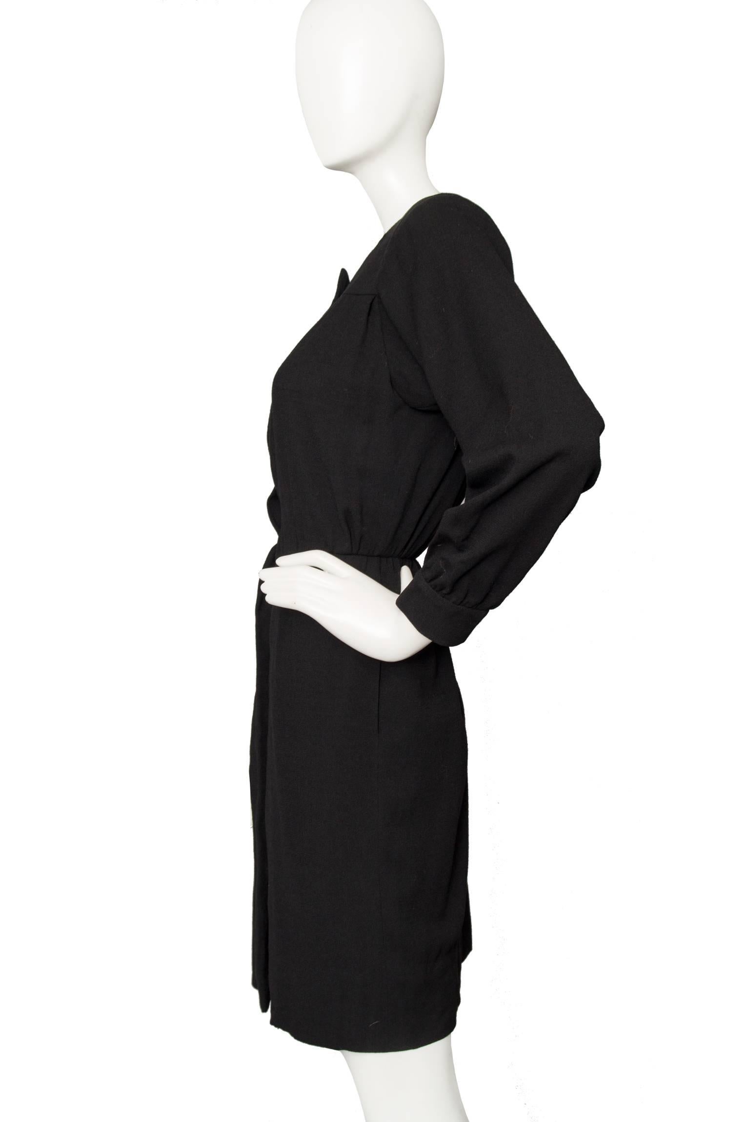 A black 1980s Yves Saint Laurent wool dress with a hidden front button closure, a large visible button at the top and long sleeves with fitted cuffs. The dress has a nipped in waist and slightly puffed shoulders with shoulder pads. 

The size of