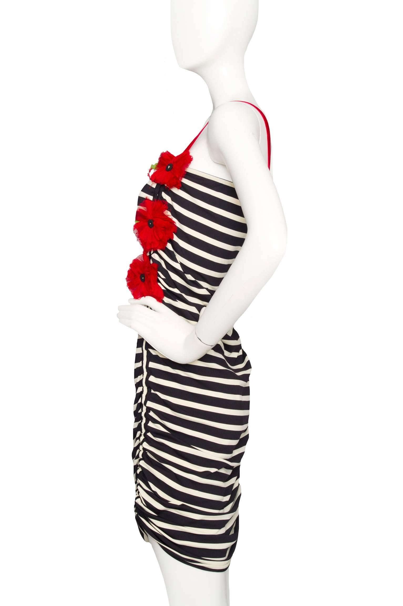 A figure-hugging 1990s Jean Paul Gaultier black and white vertical striped cocktail dress with elasticated ruching at the side. The dress has contrasting bright red velvet straps and red flower appliqué along the left side of the bust. 

The size of