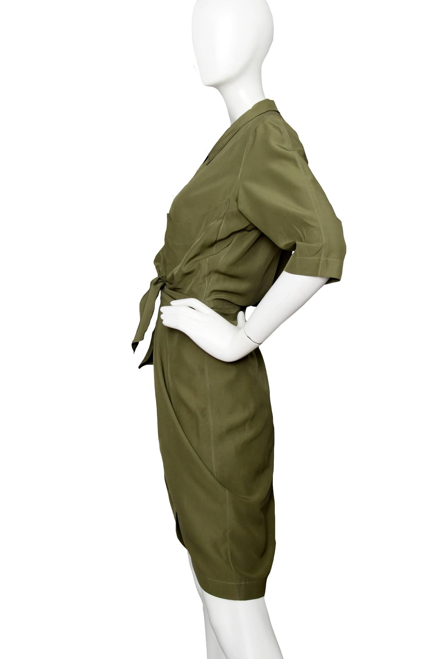 A 1980s Thierry Mugler forest green silk shirt dress with short slouchy sleeves and a button down front with a push button closure. In the center front, the blouse has a tie waist that accentuates the waistline and creates a draped effect around the