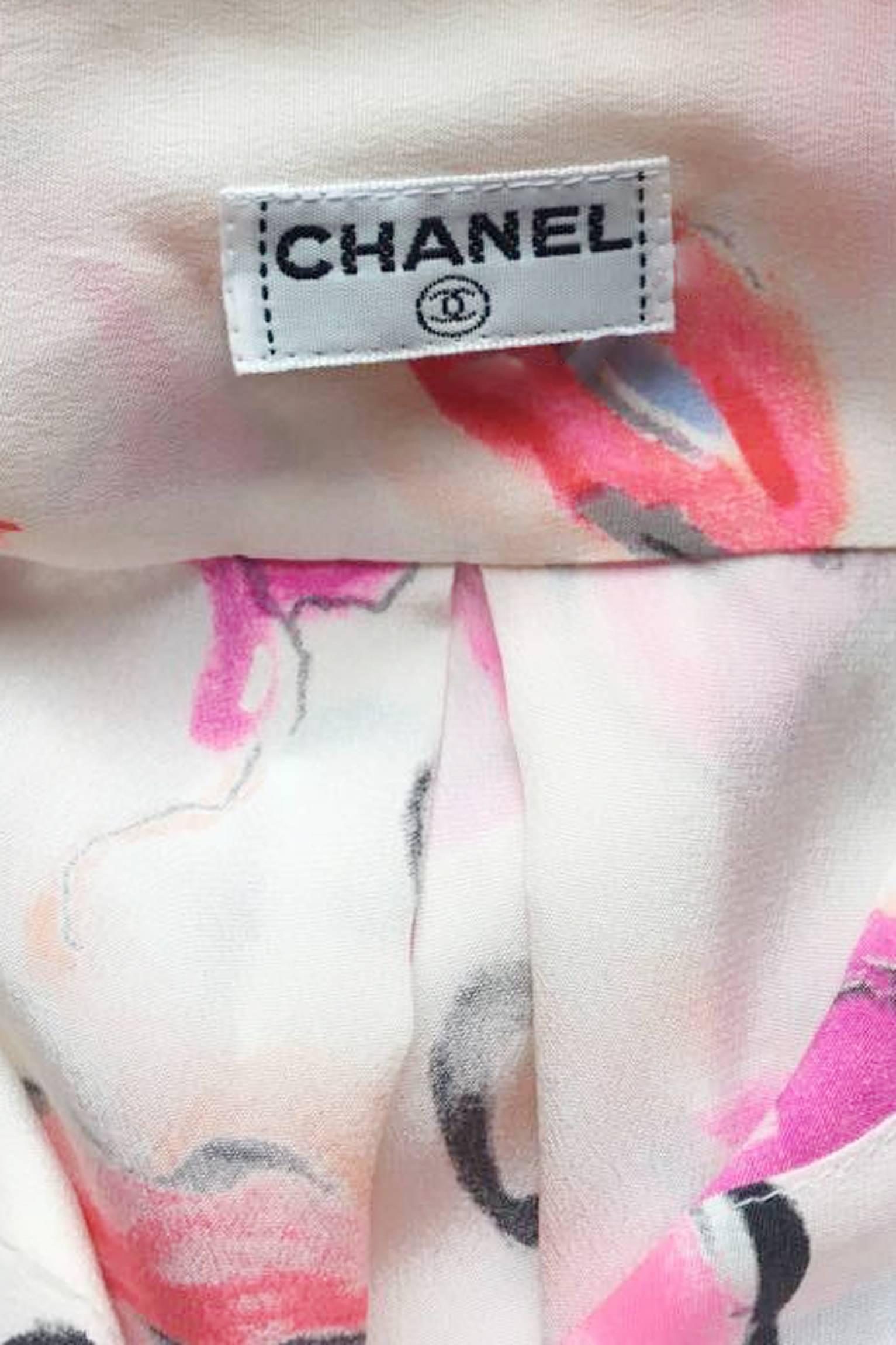 A 1980s white Chanel silk shirt with long tapered sleeves with one buttoned cuffs and a front buttoned closure. All gold colored buttons features the iconic double c logo. The shirt has a bright pink and red print portraying sassy lips with black