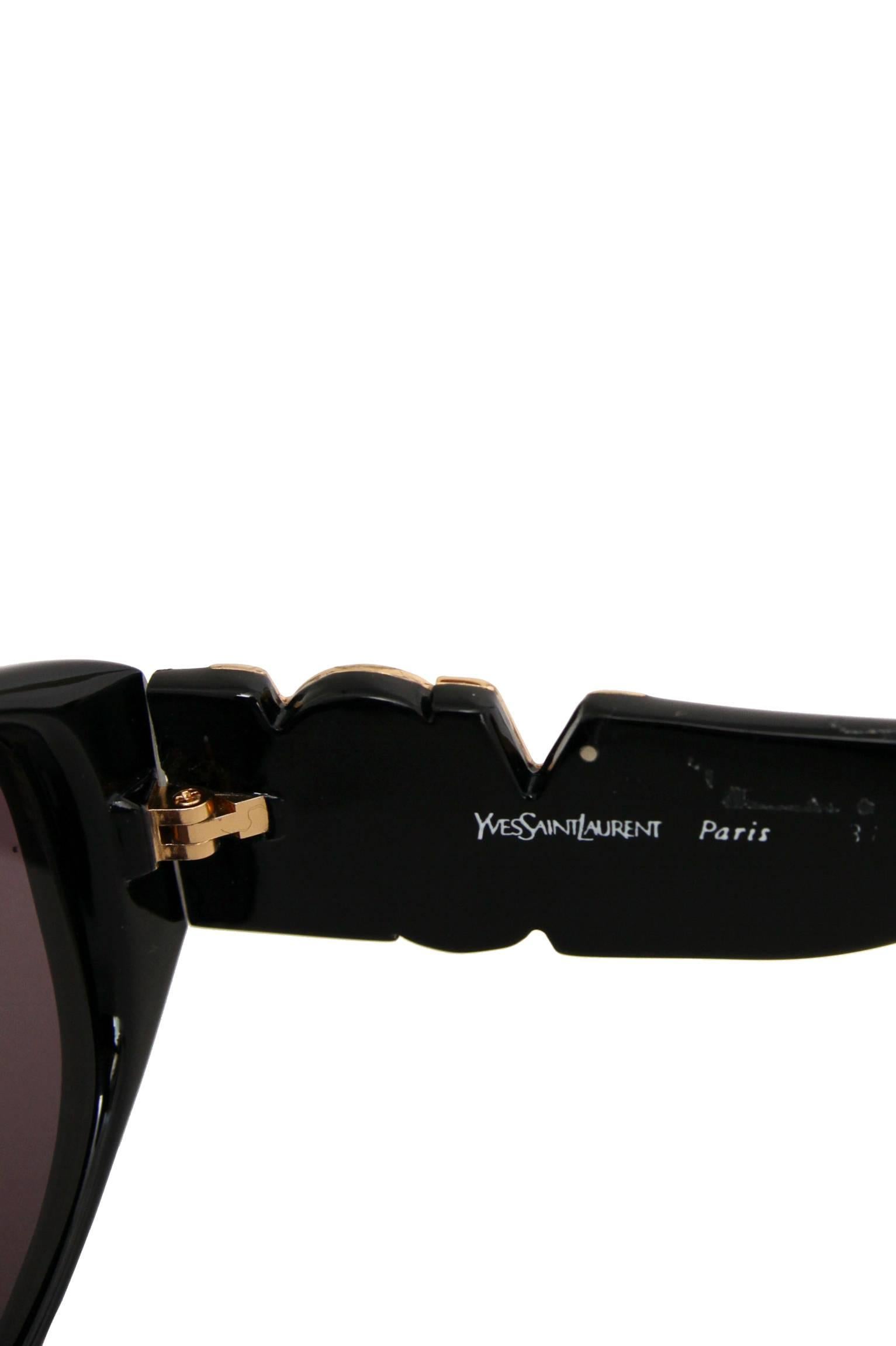 A pair of 1990s black  Yves Saint Laurent sunglasses with black lenses and a large gold toned 'YSL' detail at the top of the temple. 

The logo measures: 3x2 cm

The sunglasses have the following measurements: 
Bridge: 1.5 cm
Temple Length: 13.5