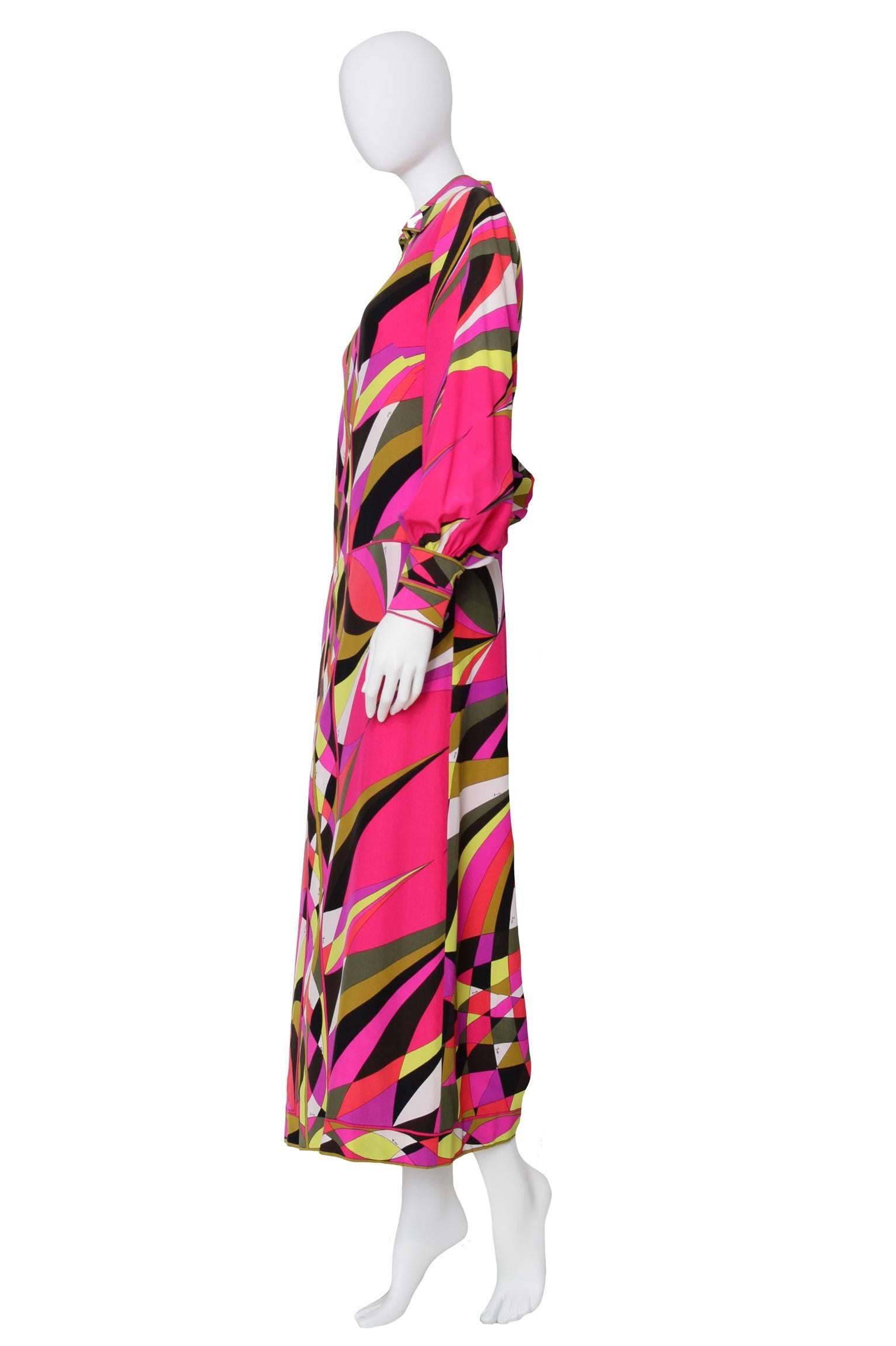 An incredible 1970s Emilio Pucci drop-waist ankle-length evening dress with a front zipper closure and double buttoned cuffs. The dress sports a multicolored graphic print which is characteristic of the house. The print is held in a bright pink