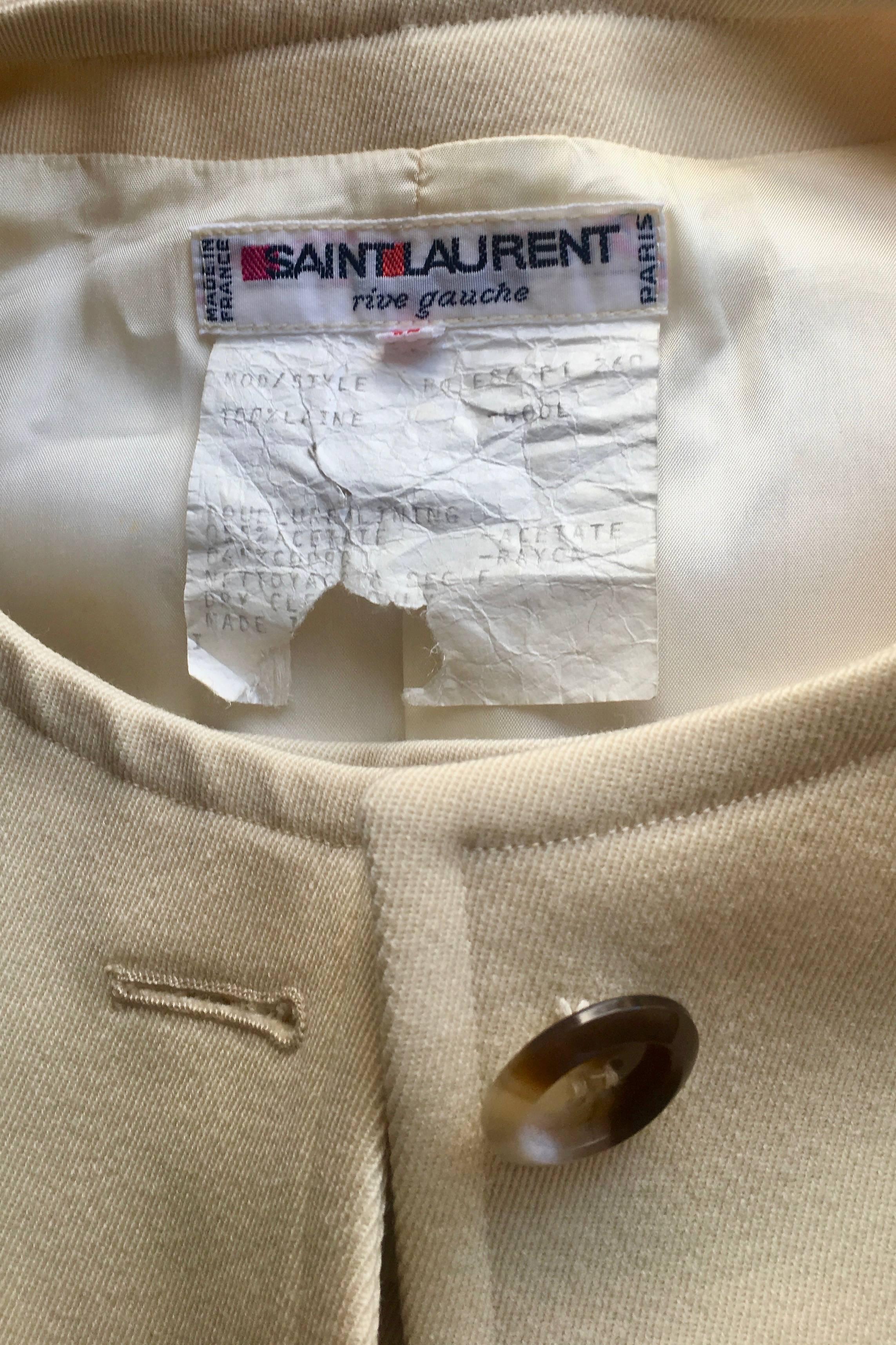 A great early 1980s Yves Saint Laurent Rive Gauche cream colored wool skirt suit, consisting of a pencil skirt with a back slit and a fitted blazer. 

The blazer has a cinched in waist and a mock flap pocket situated on each side of the waist and
