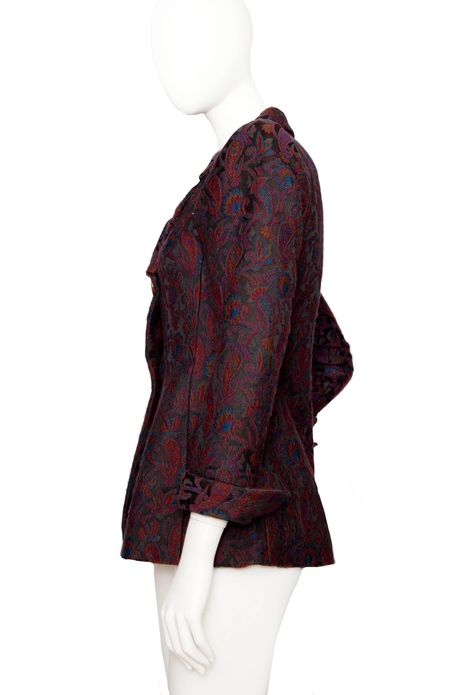 A 1980s Yves Saint Laurent Rive Gauche tapestry blazer with an asymmetrical front buttoned closure and long tapered sleeves with turn up cuff. The color of the tapestry pattern consists of a dark burgundy and blue colors intertwined to form a