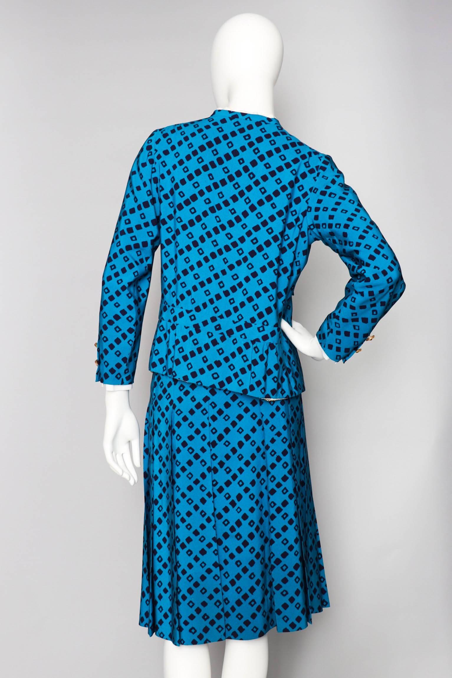 A stunning 1960s bright blue Chanel silk skirt suit with black graphic print consisting of a pleated skirt and fitted jacket. The jacket has a rounded neckline with a white ruffled and detachable cotton collar and white detachable cuffs. In the