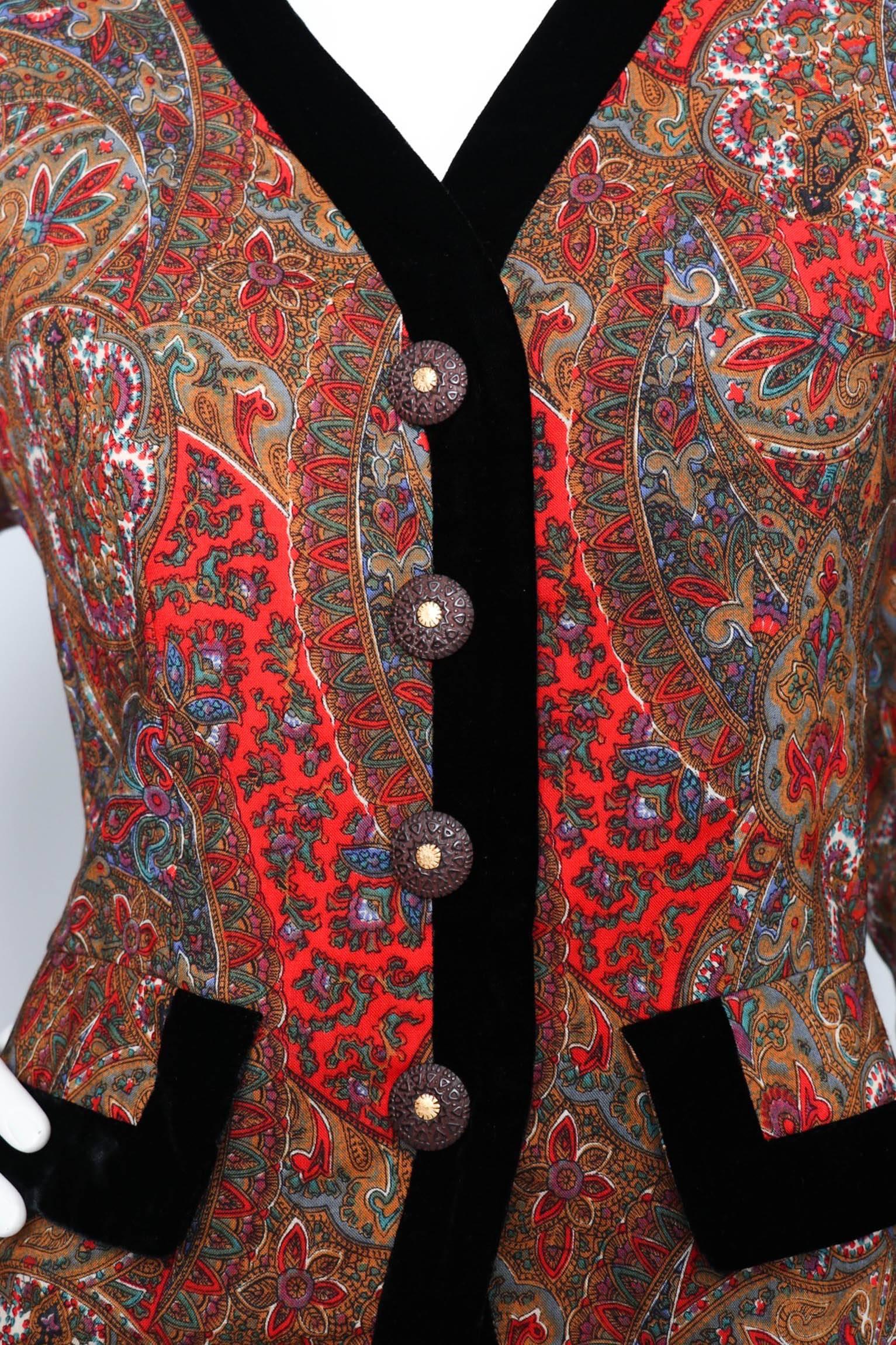 A beautiful 1980s vintage Yves Saint Laurent blazer with wide shoulders and a nipped-in waist. The blazer is clad in a paisley print held in a red, blue, green and yellow colors with white accents. A black velvet trim is wrapped around the collar,