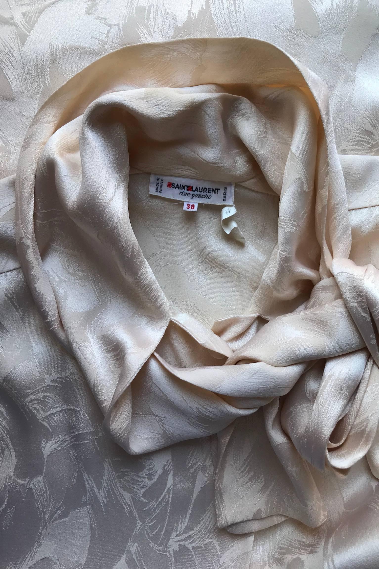 A fabulous 1980s Yves Saint Laurent Rive Gauche ivory silk blouse with long sleeves, one button cuff and a front button closure. The blouse has a beautiful jacquard woven feathers and a bow collar. 

The size of the blouse corresponds to a modern