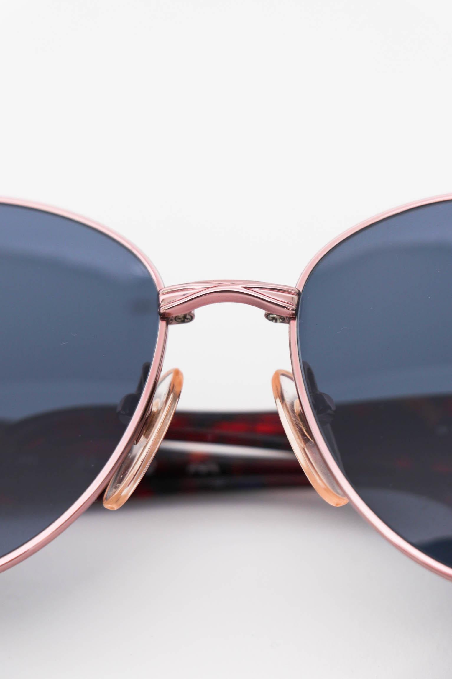 A pair of 1980s Yves Saint Laurent sunglasses with red temples,  blue tinted glasses and gold& silver hardware. The glasses are attached by an ornamental detail that incorporates the YSL logo. 

The sunglasses have the following measurements:
Temple