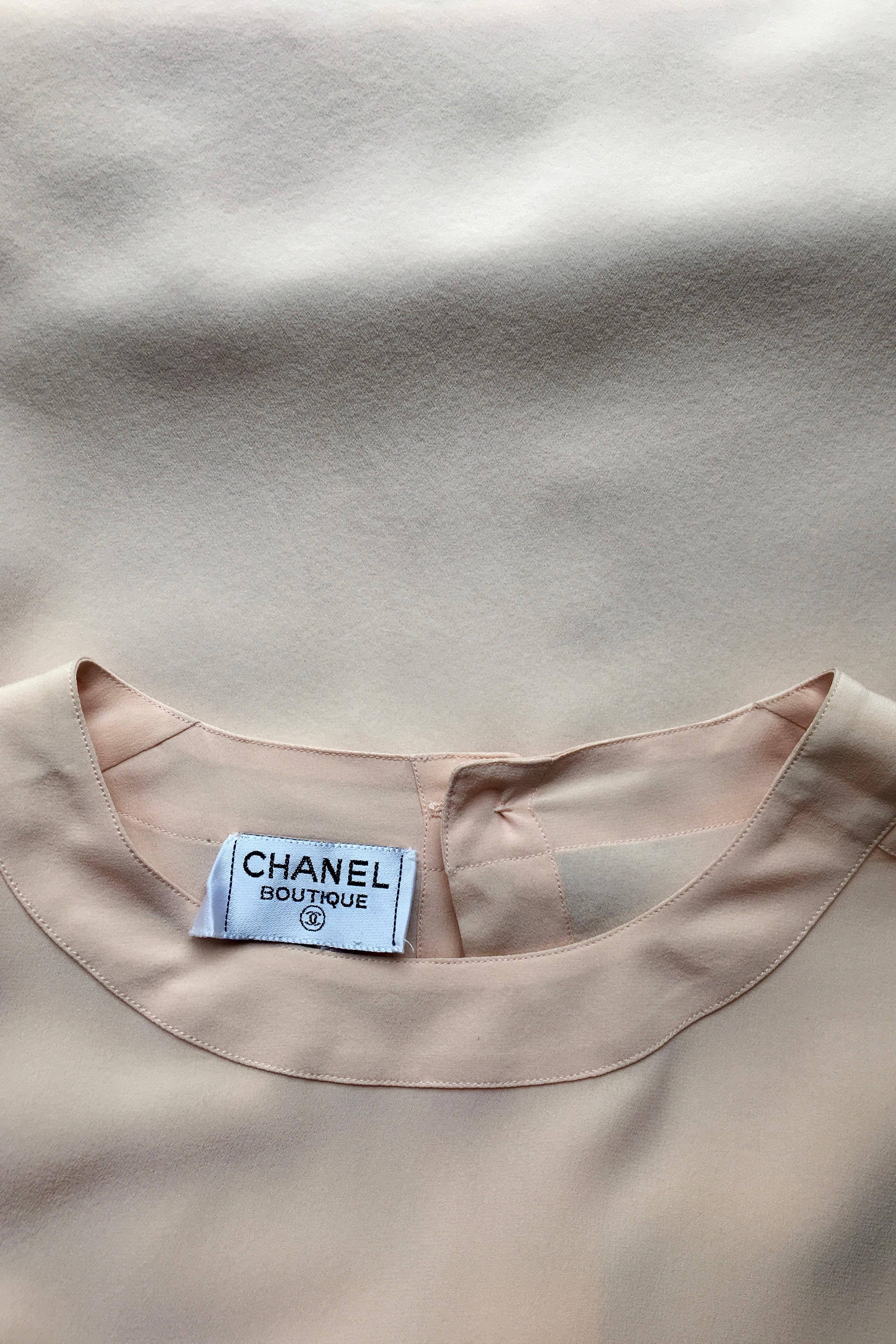 A classic 1980s Chanel baby pink colored silk blouse with short sleeves, a round neckline and patch pockets situated on both sides of the bust. The boxy fit gives a relaxed feel while the gold button closures of both pockets gives an elegant edge.