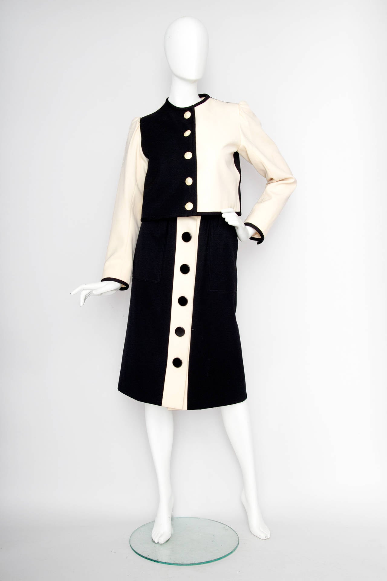 A 1980s black & off-white monochrome Yves Saint Laurent wool skirt suit consisting of a cropped boxy jacket and a high waisted pencil skirt. 

The jacket features long sleeves, a round neckline, shoulder-pads, one buttoned cuffs and a front button